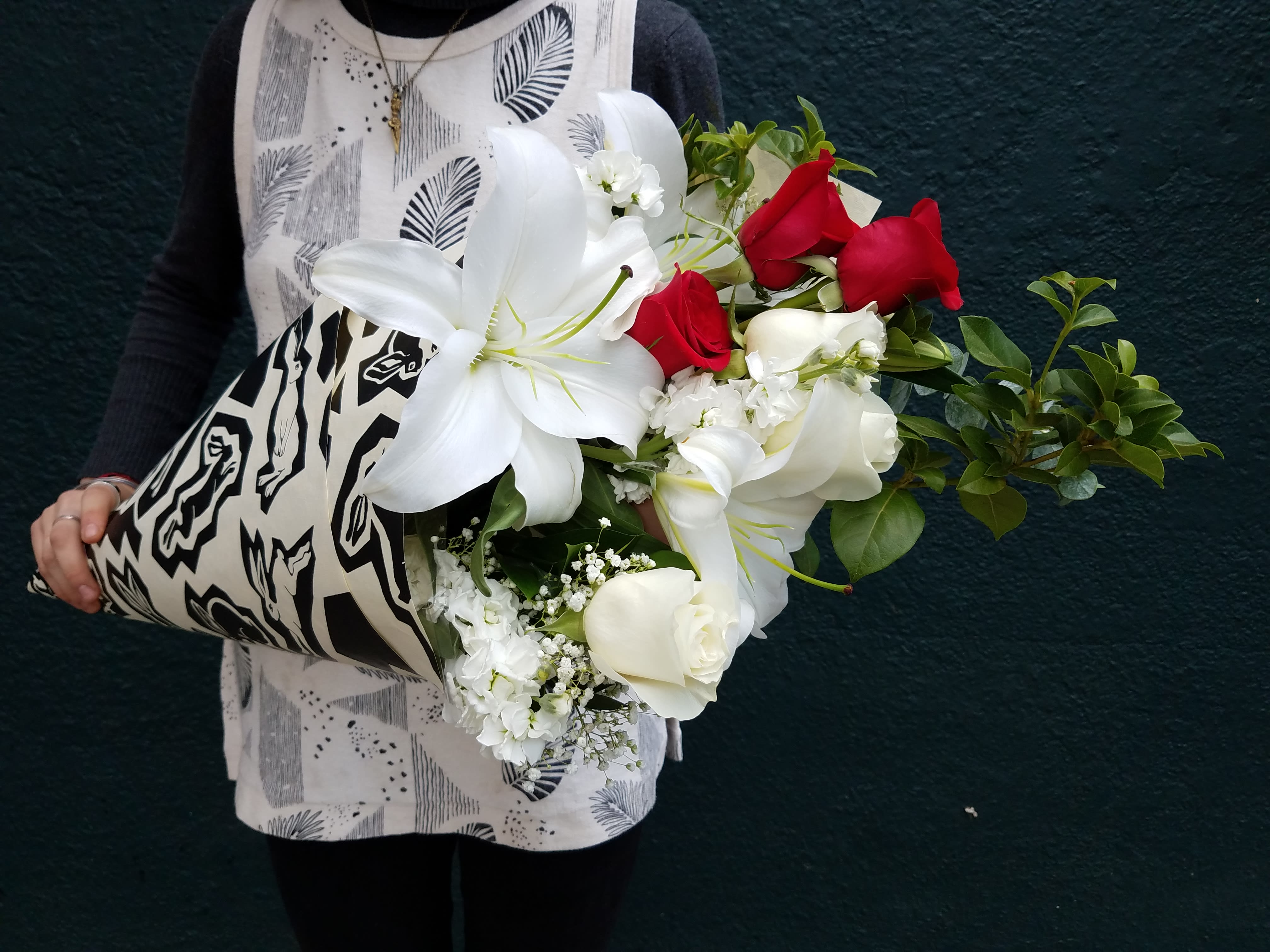 Bouquet of white lilies, red roses, and white calla lilies wrapped in patterned paper