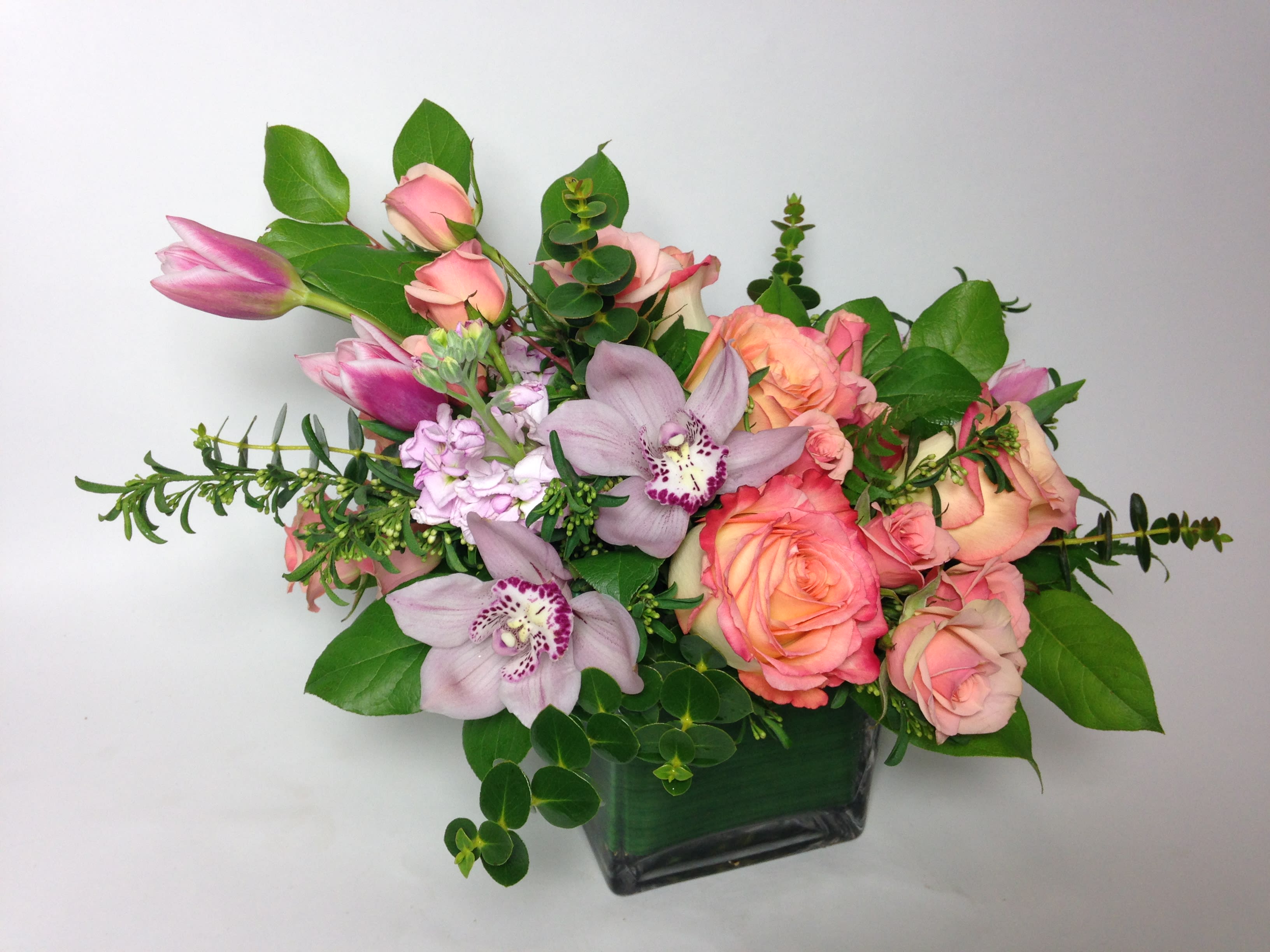 Pink roses and lavender orchids in a square glass vase