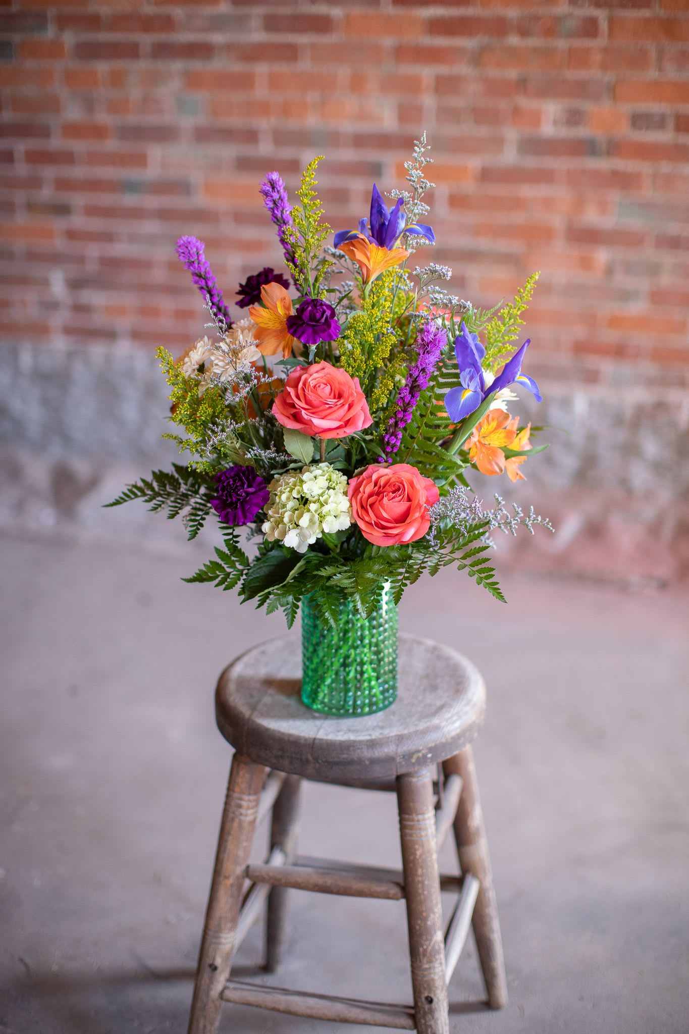 Colorful mixed bouquet in a green vase on a wooden stool