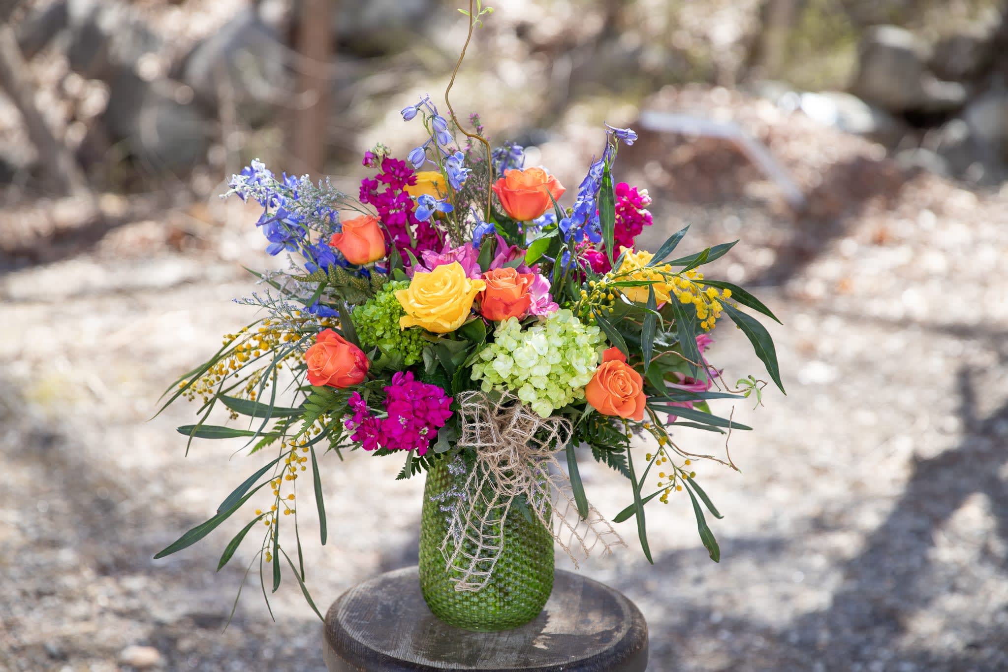 Colorful bouquet of roses, blue flowers, and hydrangea in a green vase