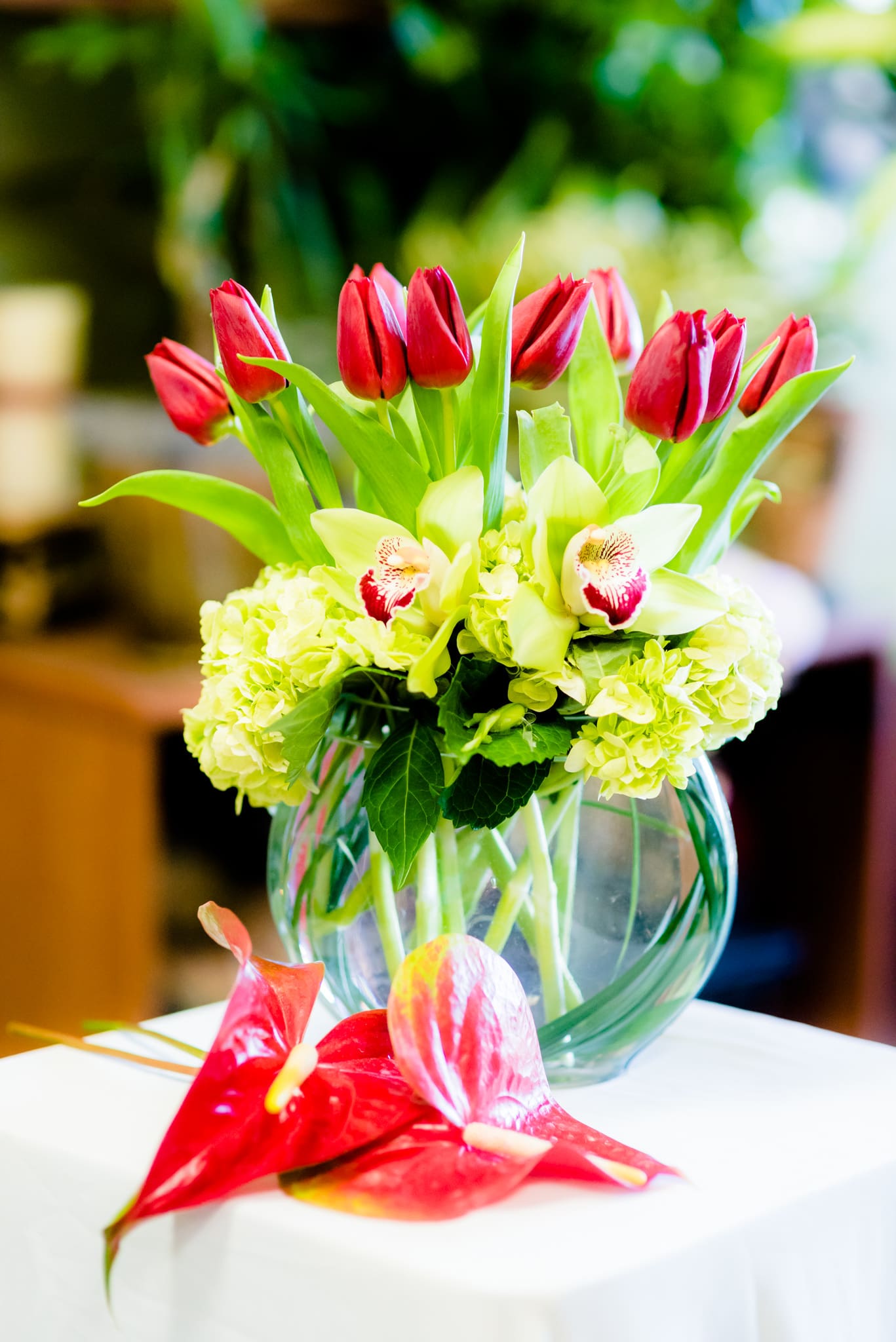 Red tulips and pale green orchids in a clear glass vase