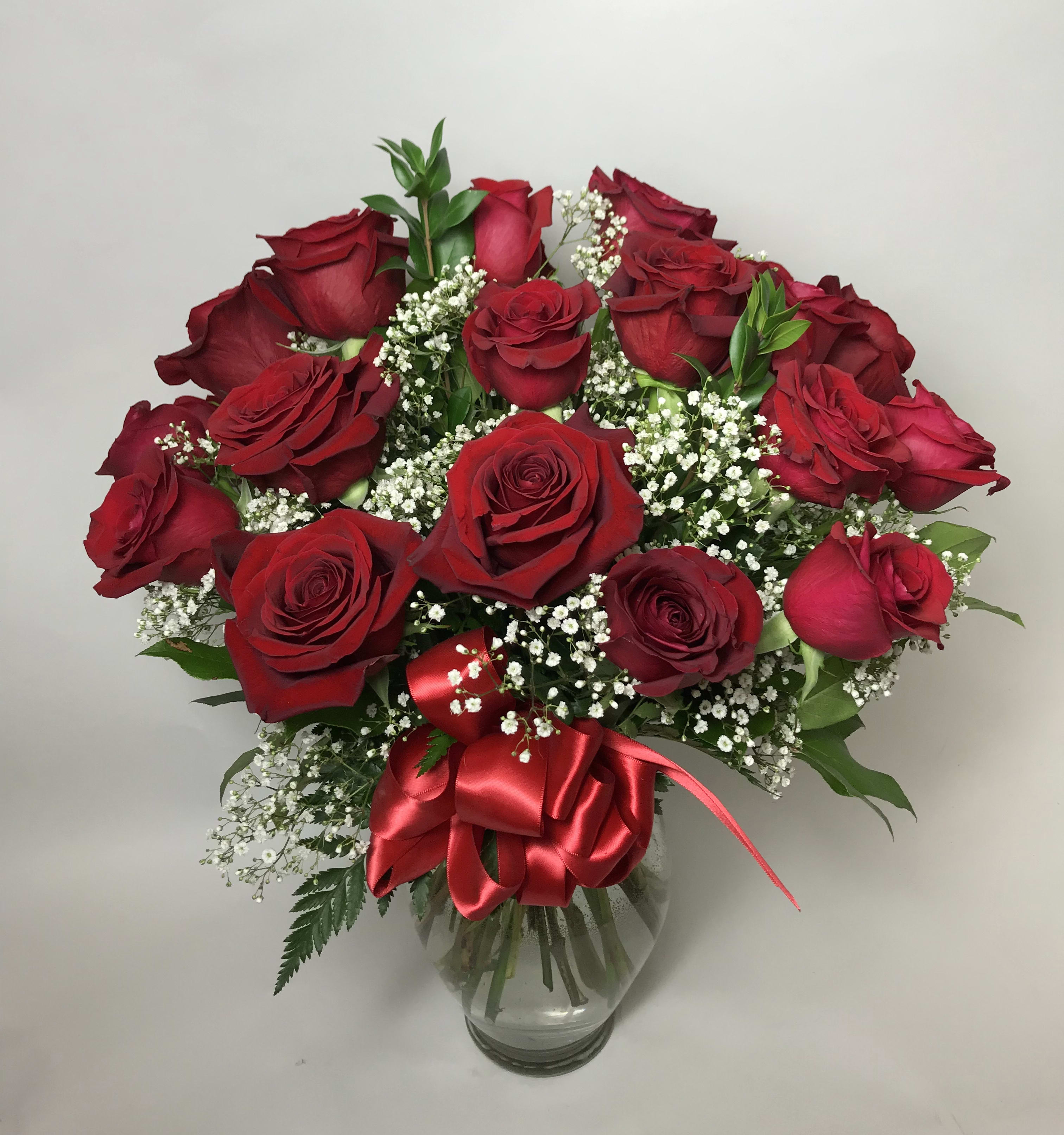 Bouquet of red roses with baby's breath in a clear glass vase and red ribbon