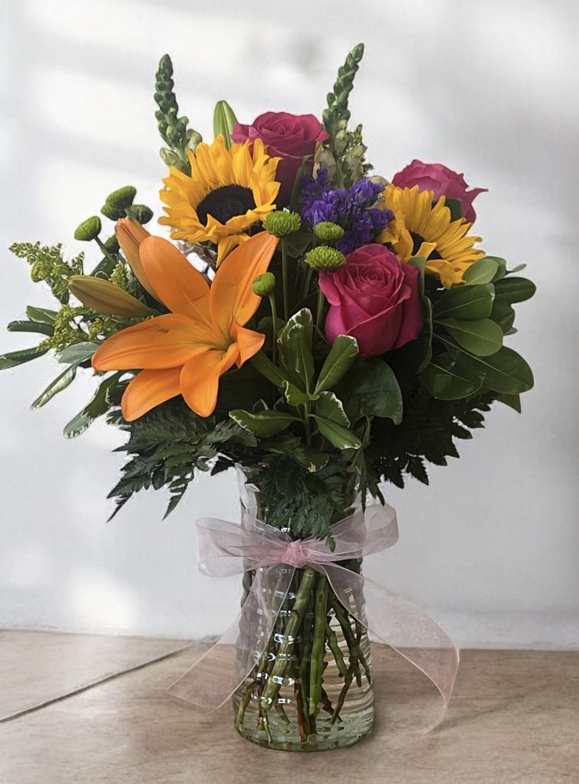 Bouquet of sunflowers, orange lilies, and pink roses in a glass vase