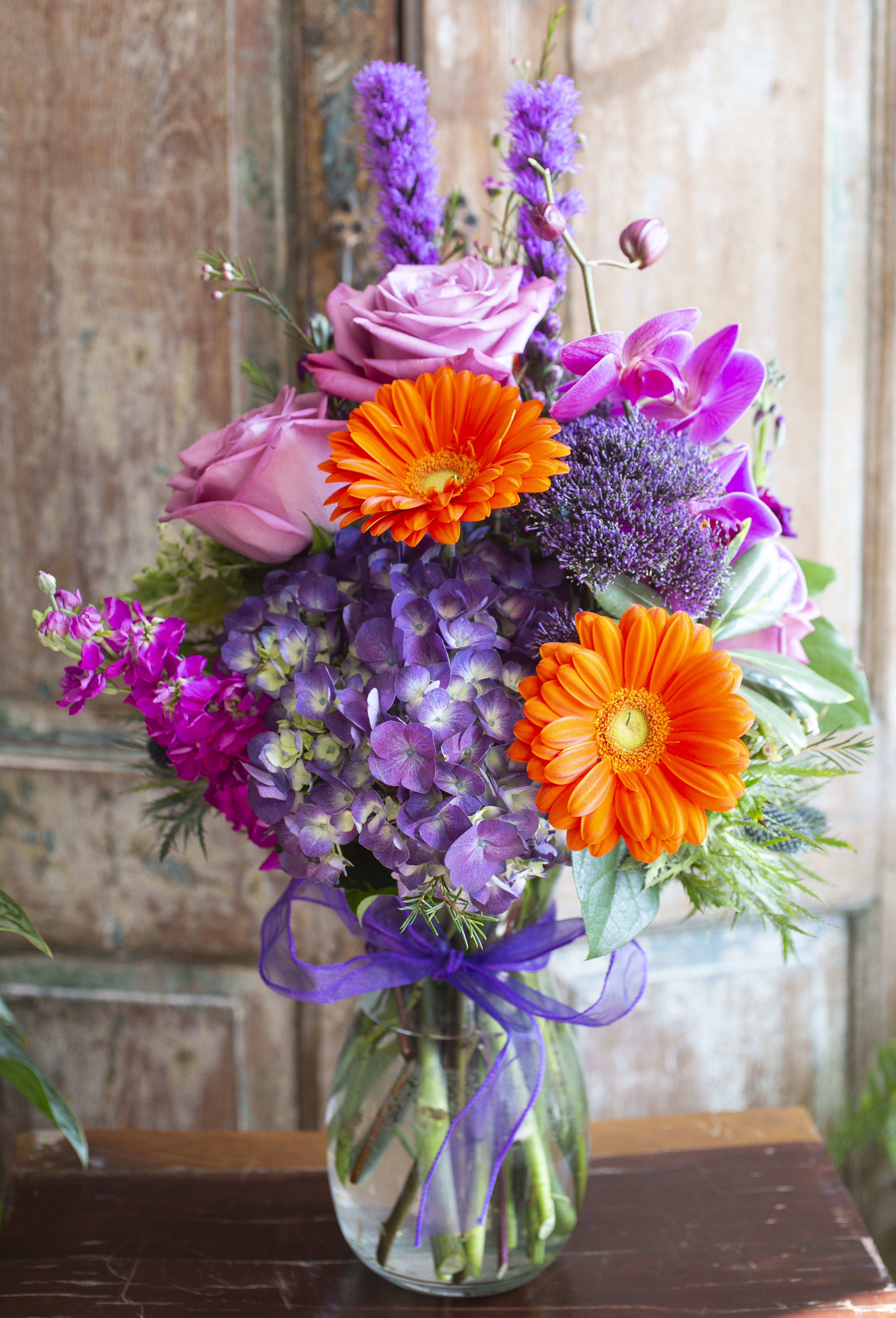 Bouquet of pink roses, orange gerberas, and purple flowers in a glass vase