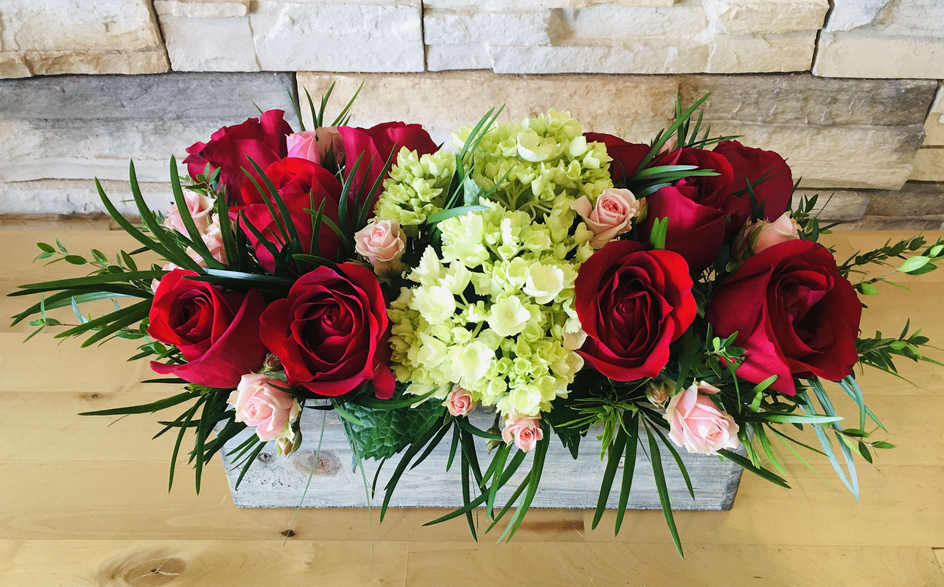 Red roses and pale green hydrangeas in a rectangular wooden box