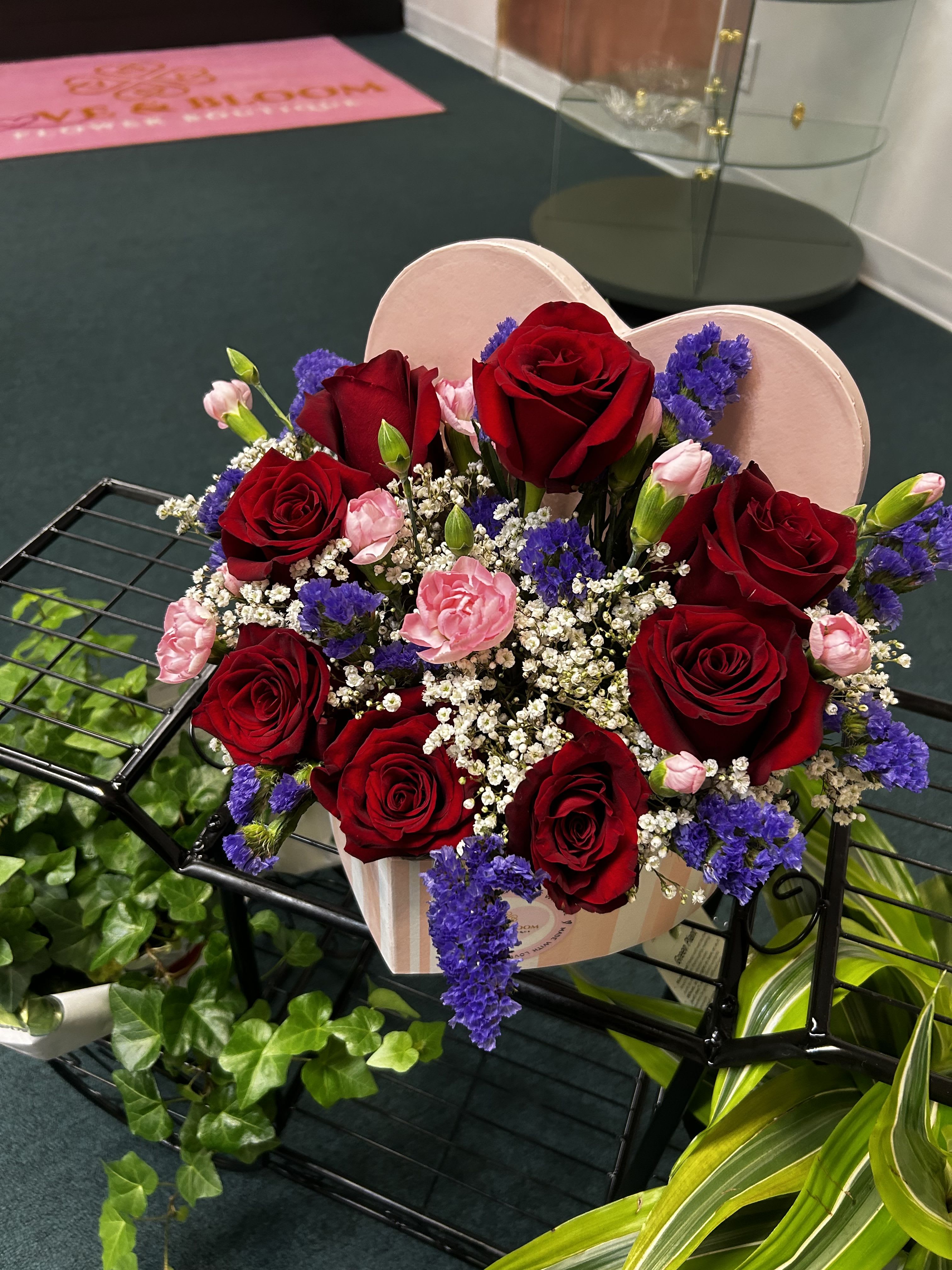 Heart-shaped box of red roses with pink carnations and purple filler flowers