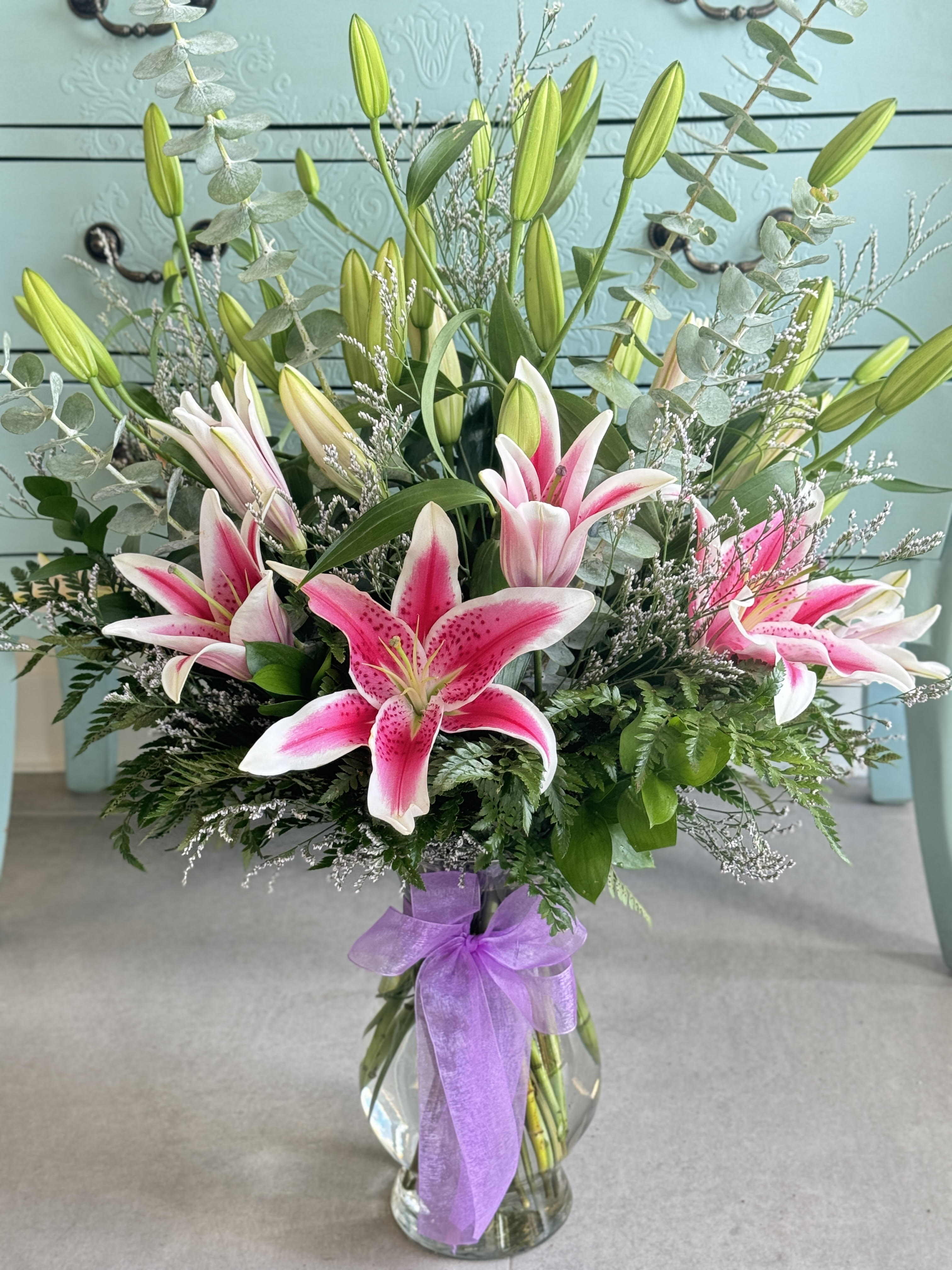 Pink stargazer lilies in a glass vase with a purple ribbon