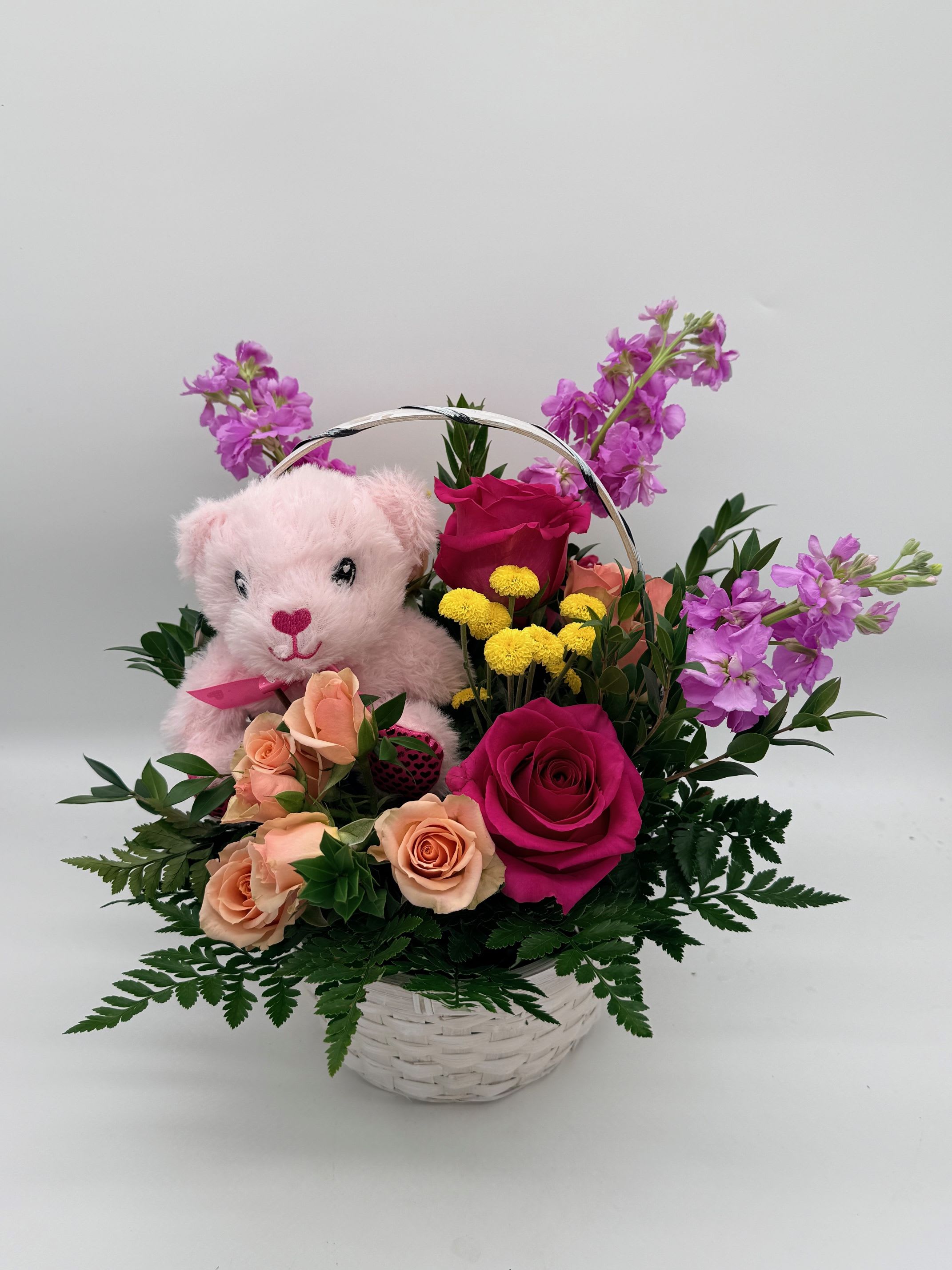 Pink teddy bear in a basket with roses and purple flowers