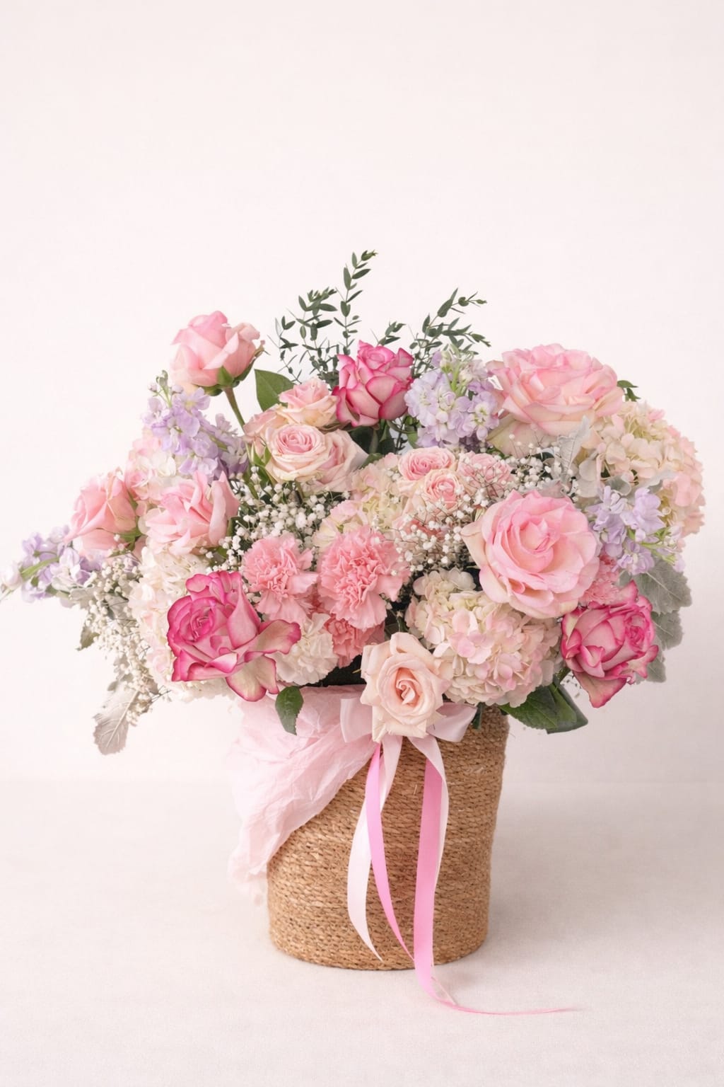 Pink and cream rose bouquet in a woven basket with ribbon