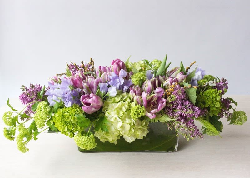 Low floral arrangement with purple, pink, white, and green blooms in a rectangular vase