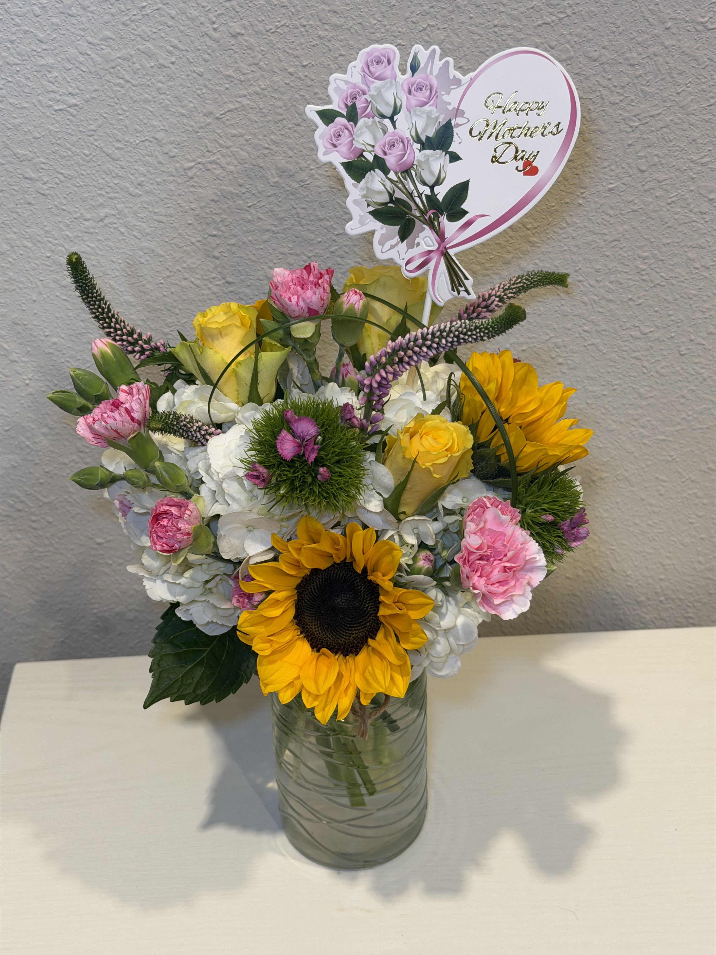 Bliss sunshine  - Bright sunflowers with pink &amp; white roses, pink carnations and white hydrangeas, purple spikes in a glass vase-cheerful, full-bodied Spring bouquet with a heart Mother's Day pick.