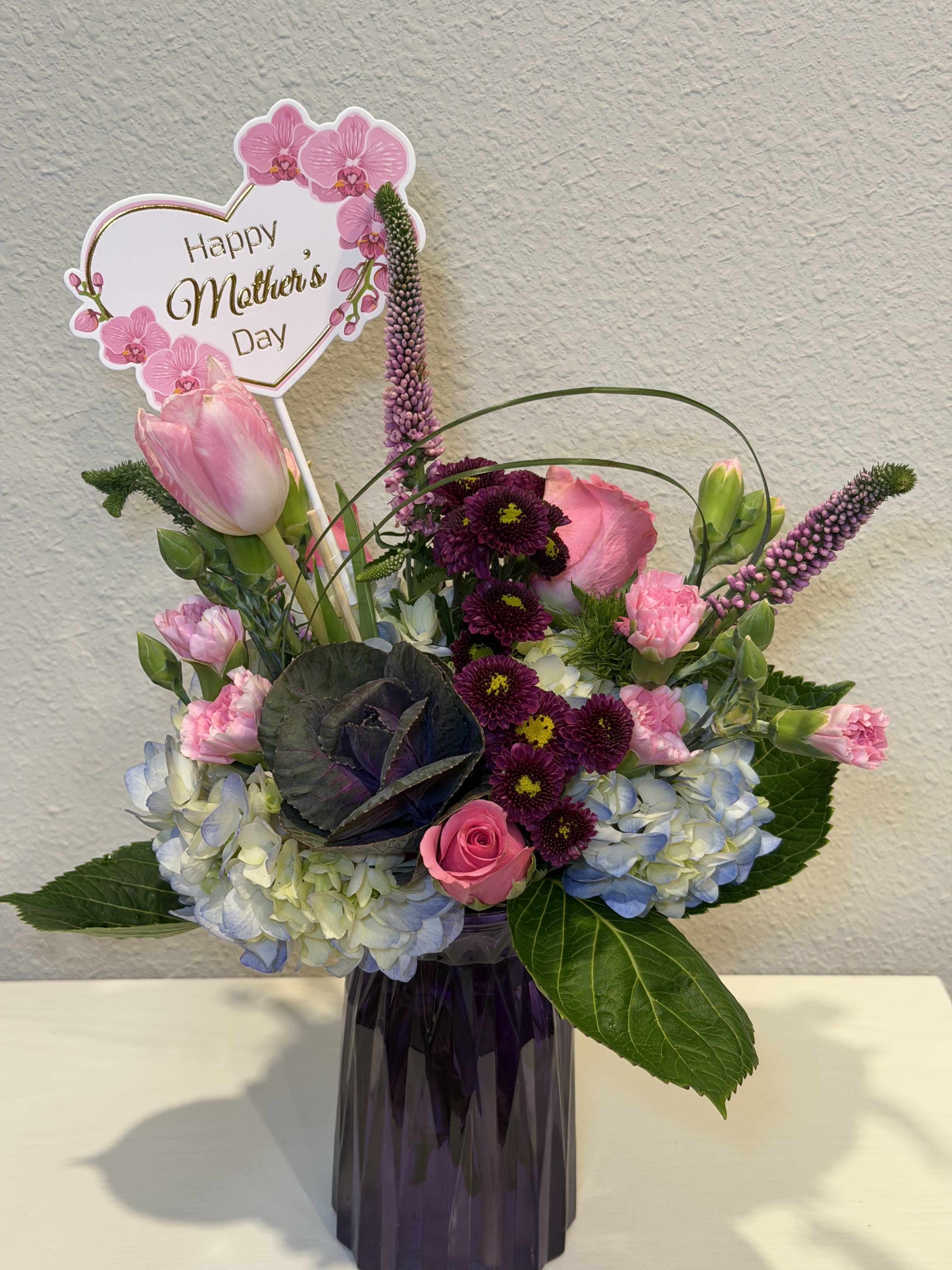 Bliss pink  - Pink and purple tulips, roses, hydrangeas and chrysanthemums arranged with white accents and greenery in a dark vase, topped with a Mother's Day sign-cheerful, romantic, gift-ready