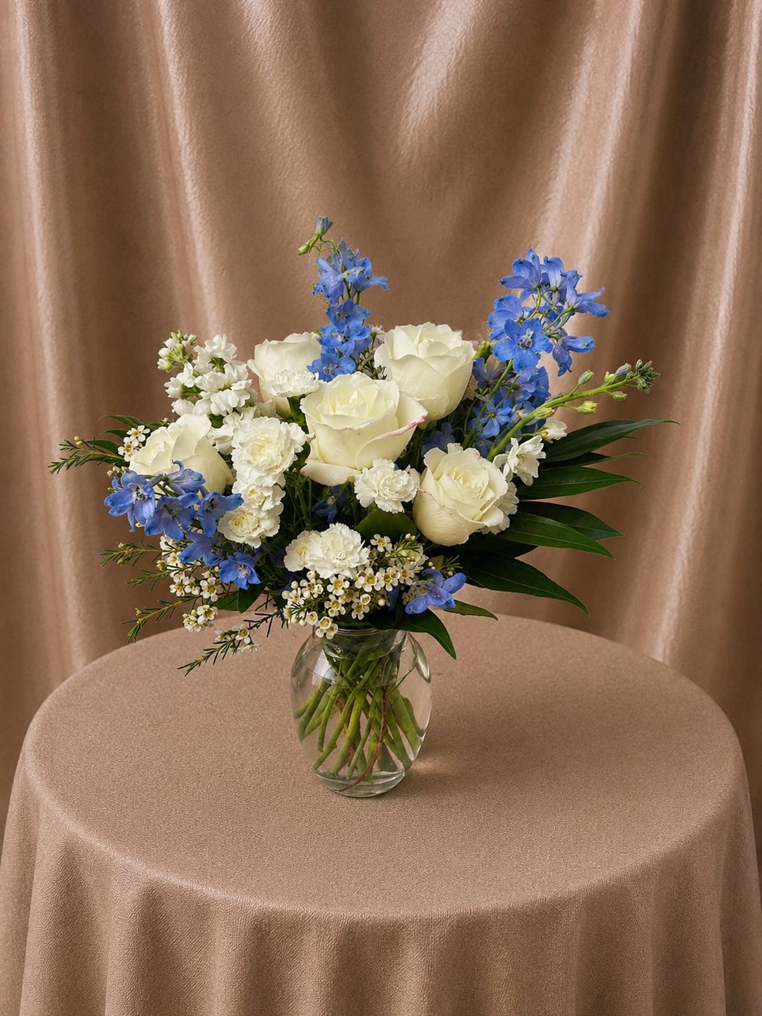 Elegant Blue &amp; Ivory Garden Bouquet - A refined hand-designed flower arrangement featuring premium ivory roses accented with soft blue delphinium, white carnations, delicate waxflower, and lush seasonal greenery. Beautifully arranged in a clear glass vase, this design blends freshness, elegance, and natural movement—creating a timeless and graceful floral gift.  Each arrangement is Designer’s Choice, thoughtfully created with fresh seasonal blooms. Flower varieties and color tones may vary based on availability while preserving the overall style, palette, and quality.  Perfect for birthdays, sympathy, thank you gestures, get well wishes, welcoming a new baby, thinking of you, Mother’s Day, or adding a refined touch to home décor.  Same day flower delivery available in Southwest Florida, including Naples, Bonita Springs, and Fort Myers Beach.