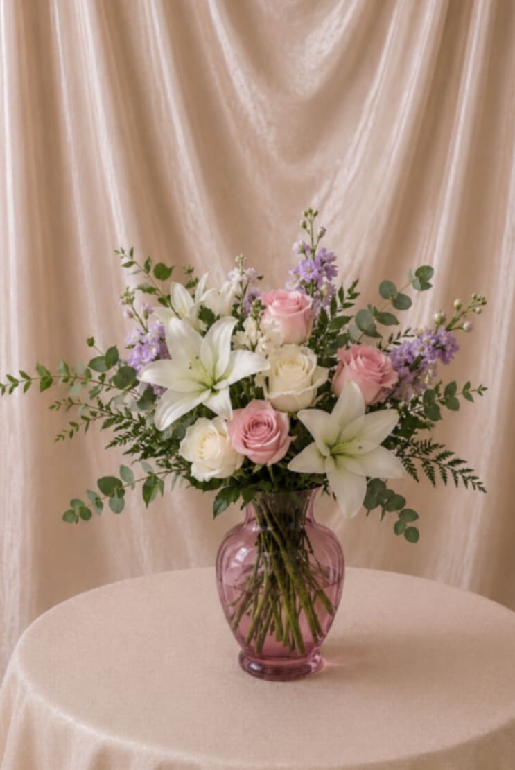 Blush Lily Garden Vase - Soft, elegant, and timeless, this fresh floral arrangement features white lilies, blush pink roses, white roses, lavender stock, eucalyptus, and seasonal greenery designed in a pink glass vase. Its natural garden-style design creates a romantic and sophisticated look perfect for celebrating life’s sweetest moments.  Perfect for gifting, home décor, birthdays, anniversaries, and especially Mother’s Day flowers delivery in Naples, Bonita Springs, Fort Myers Beach, and Southwest Florida.  Each arrangement is handcrafted with fresh flowers and designed to maintain the overall color palette, style, and quality while allowing for seasonal substitutions when necessary.  Best For: Mother’s Day, Birthday, Thinking of You, Get Well, Sympathy, Anniversary, Elegant Home Décor, Spring Floral Gift