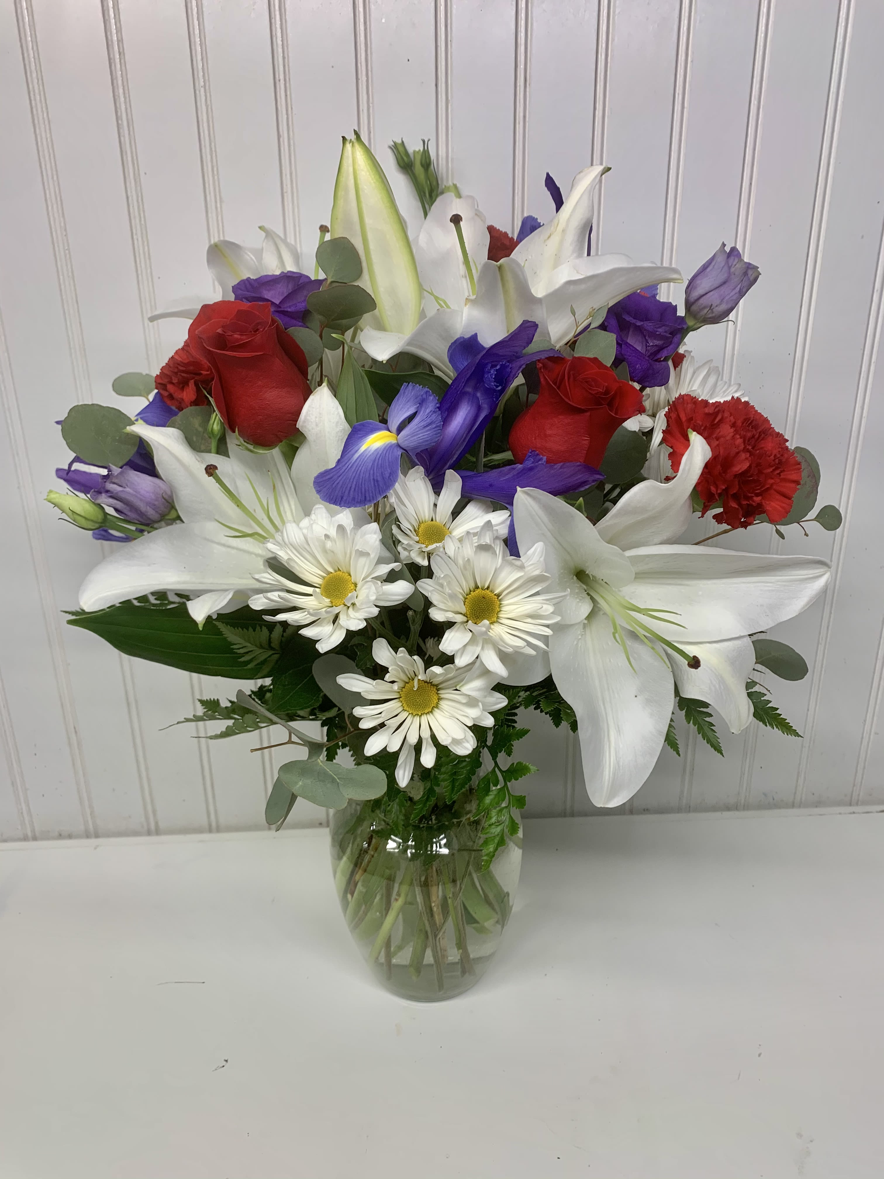 Mixed bouquet of red roses, white lilies, and daisies in a glass vase