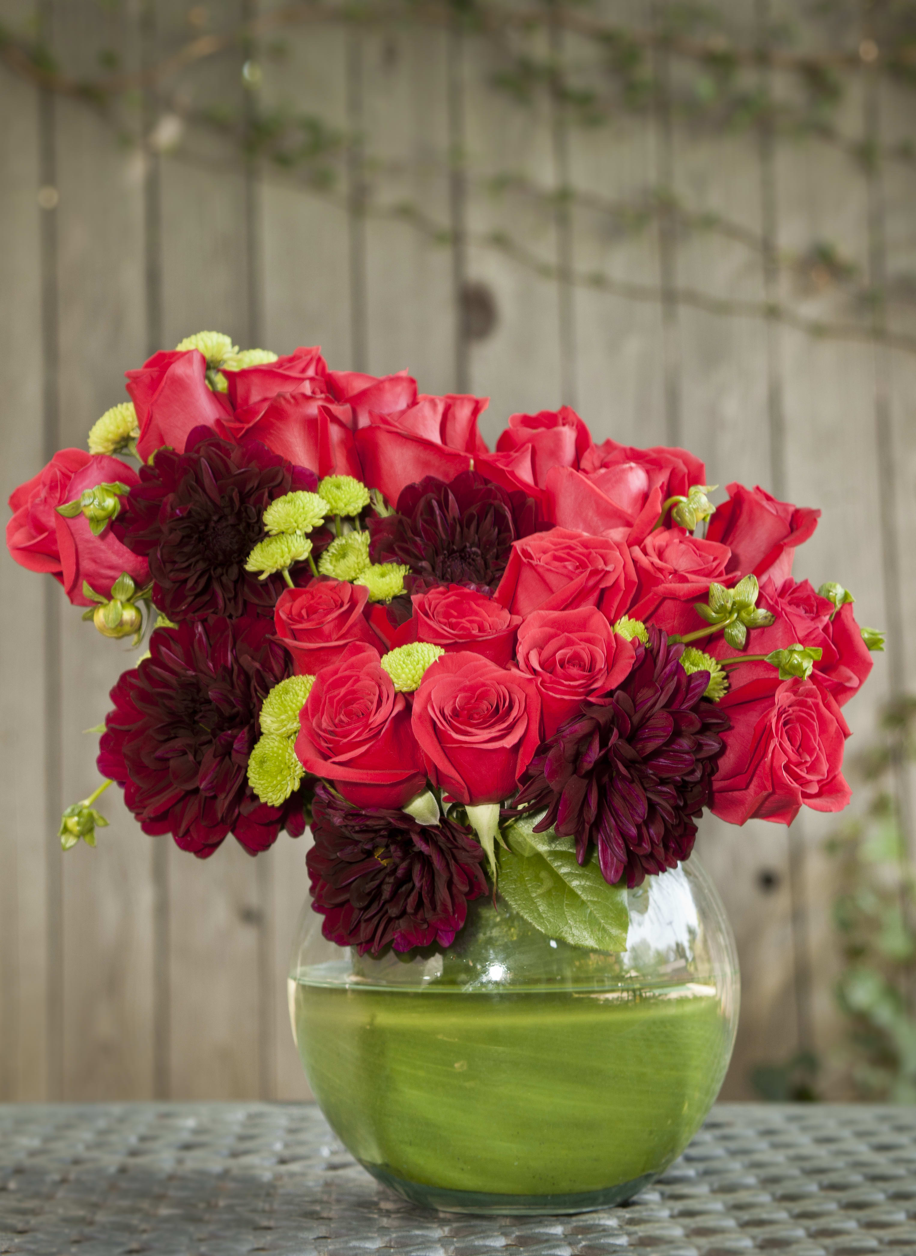 Red roses and dark burgundy blooms in a round glass vase