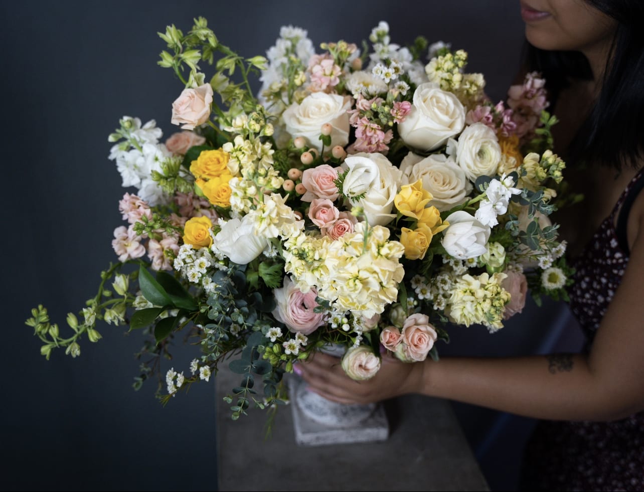 Large bouquet of white, pink, and yellow flowers held by a person