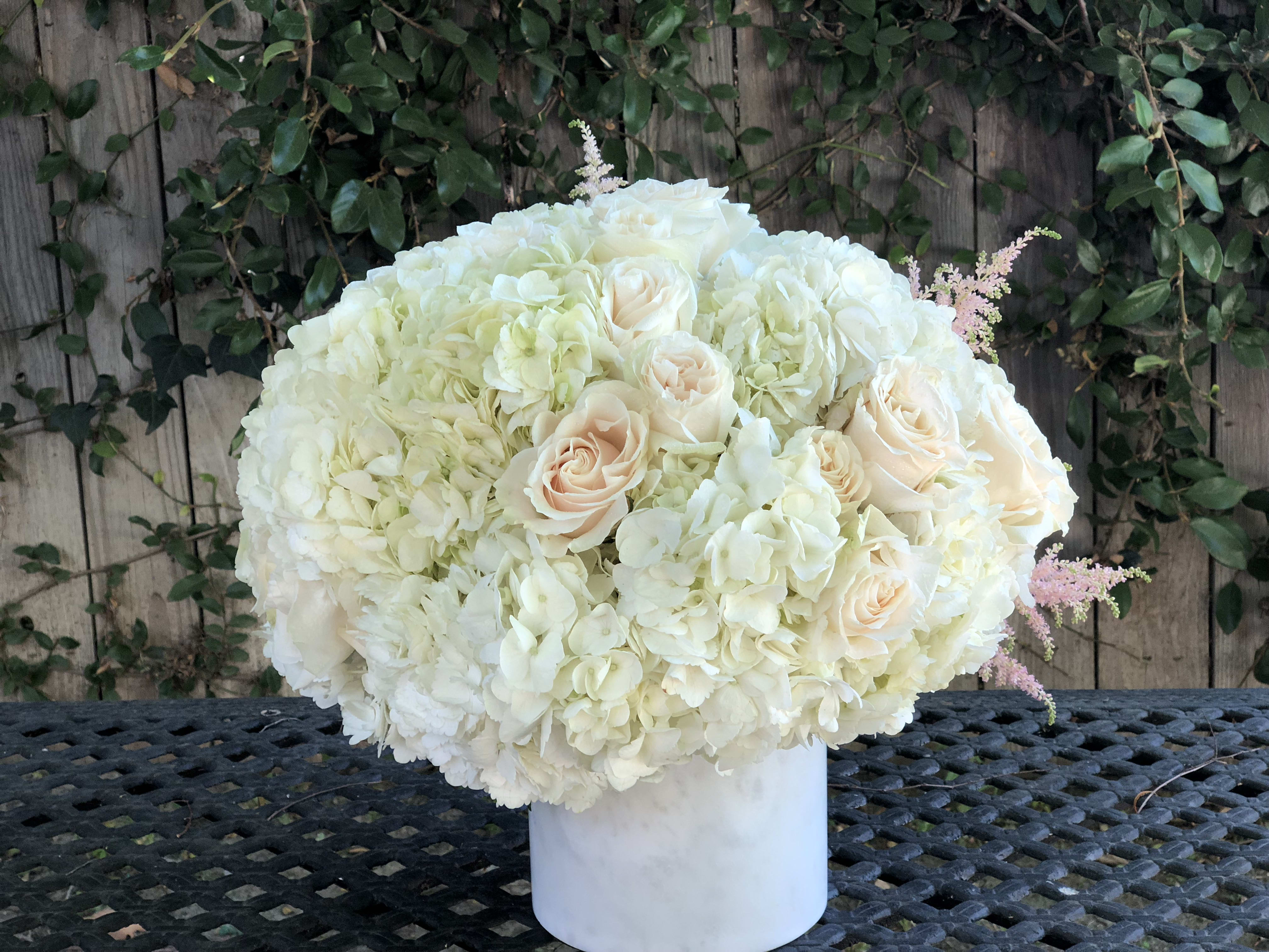 White hydrangea and blush rose arrangement in a white vase