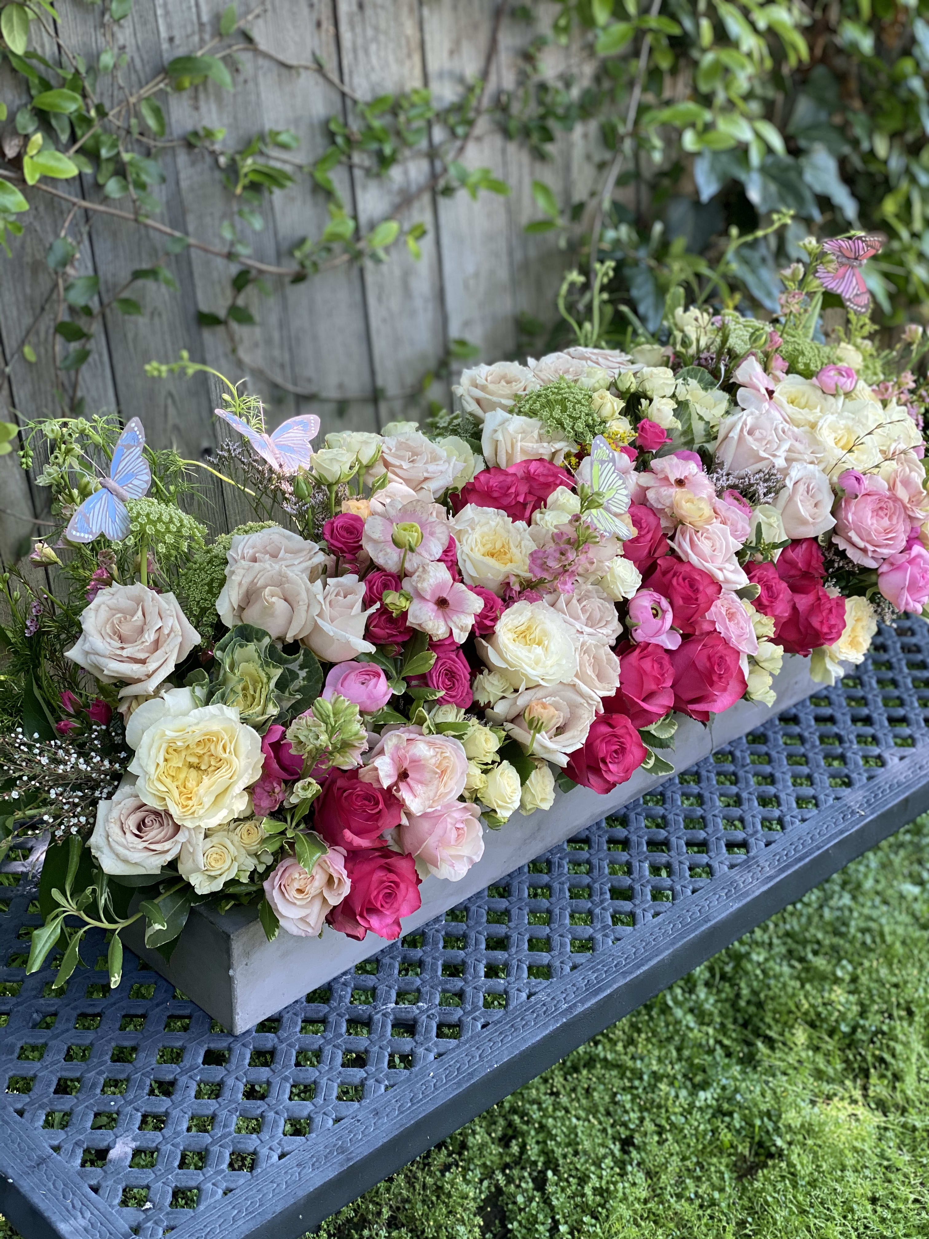 Long floral centerpiece of pink and cream roses with butterfly accents