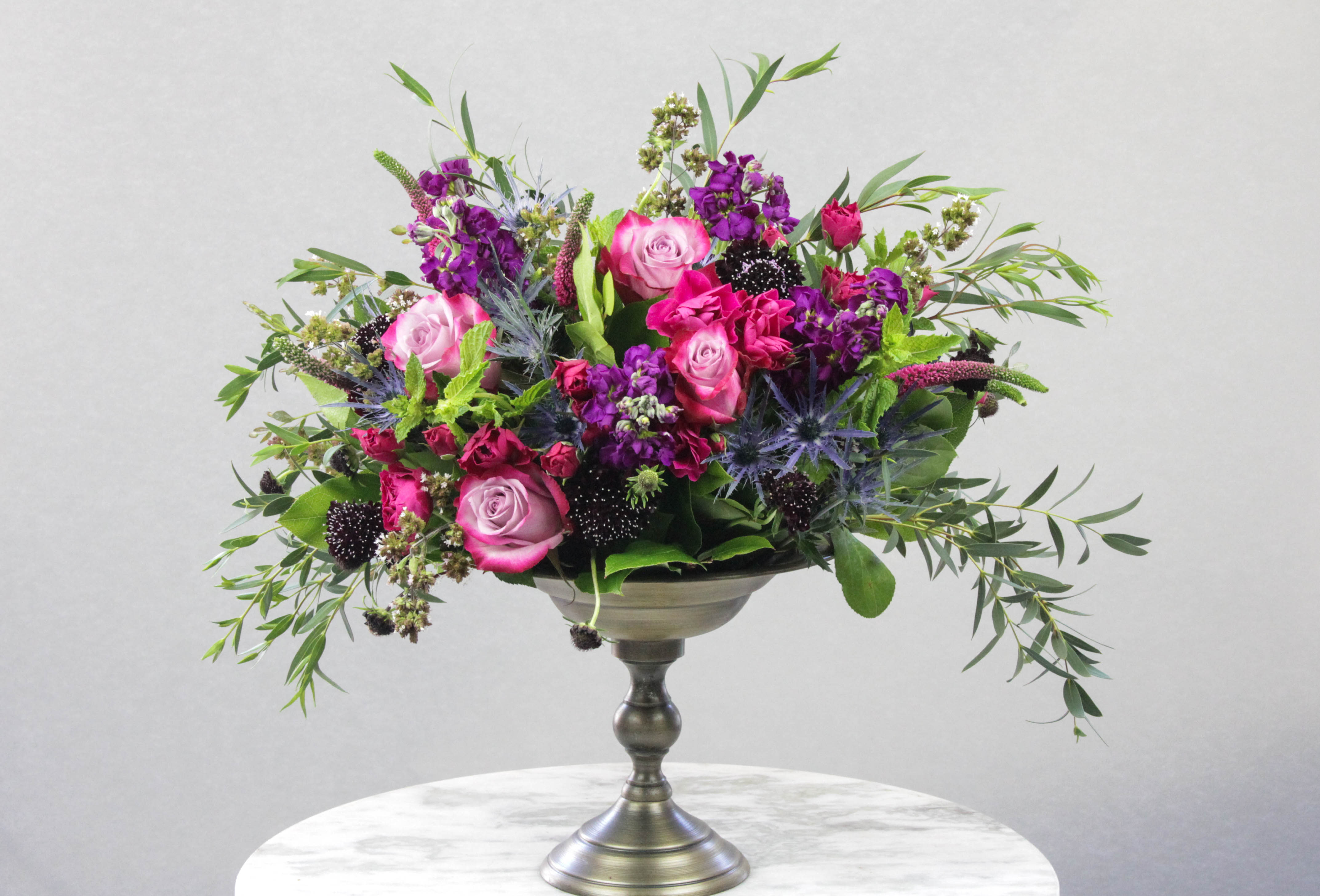 Pink and purple rose arrangement in a silver pedestal vase