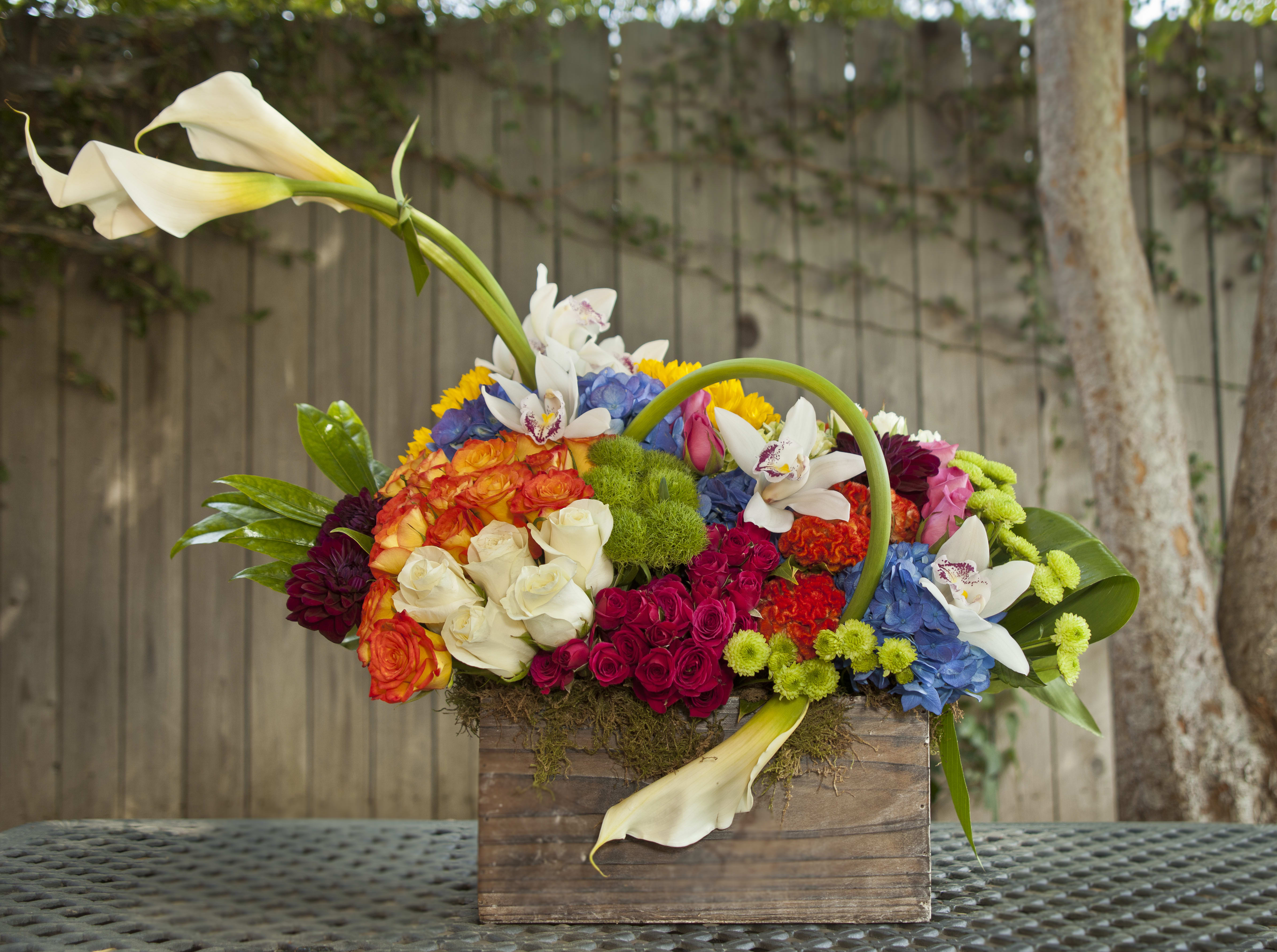 Colorful floral arrangement in a wooden box with white calla lilies