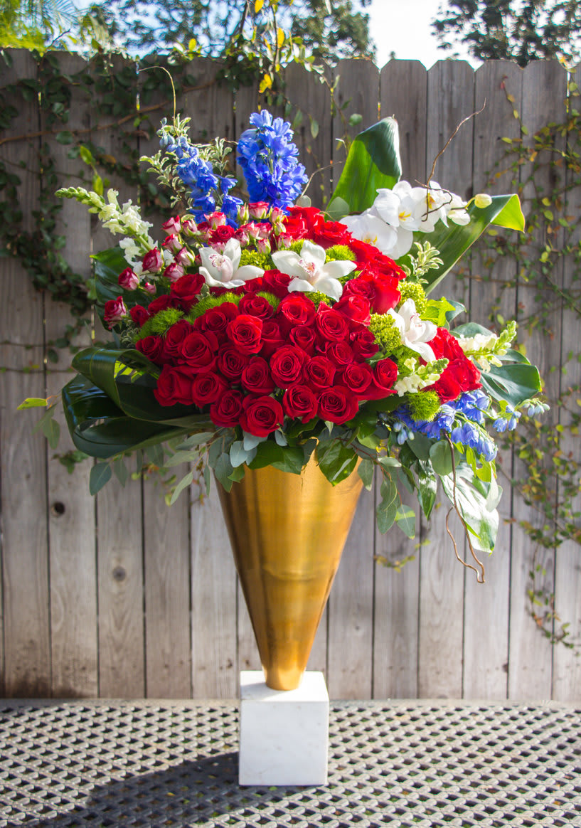 Large red rose arrangement in a gold vase with white and blue flowers