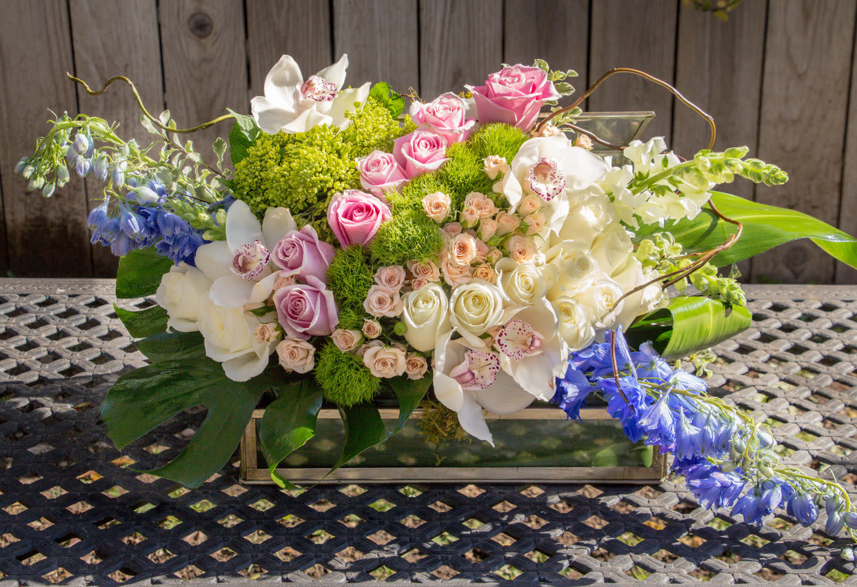 Mixed floral arrangement in a rectangular glass vase with pink, white, and blue blooms