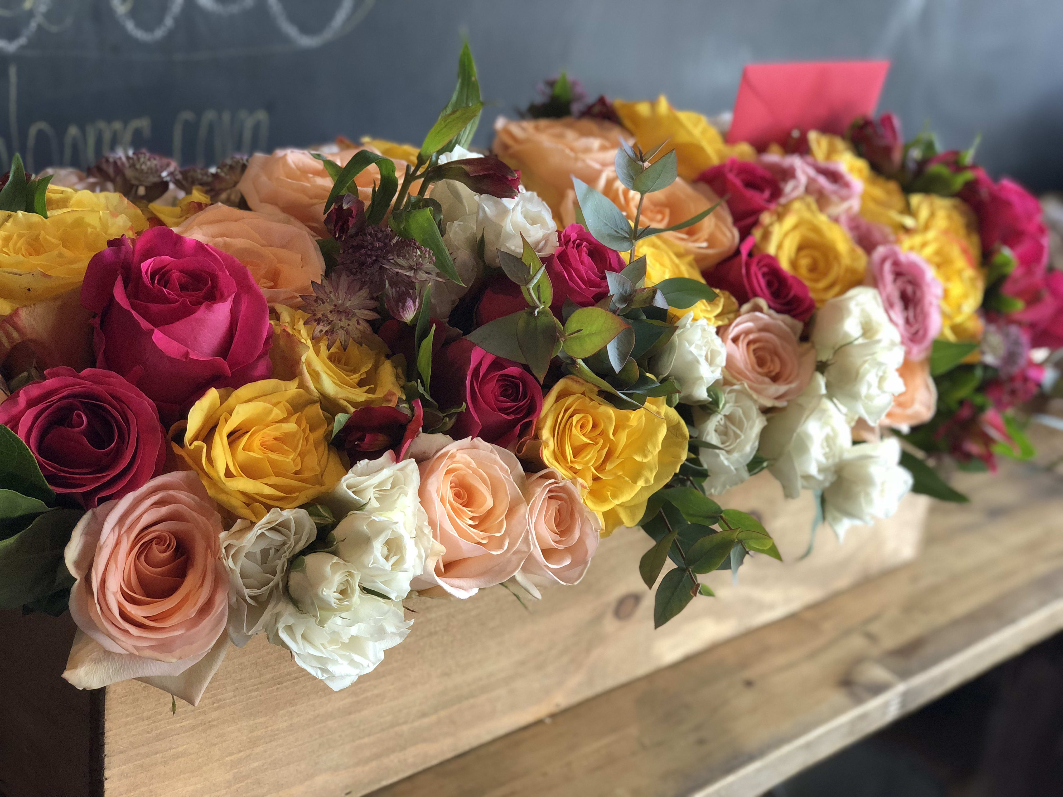 Long box arrangement of roses in pink, yellow, peach, and white