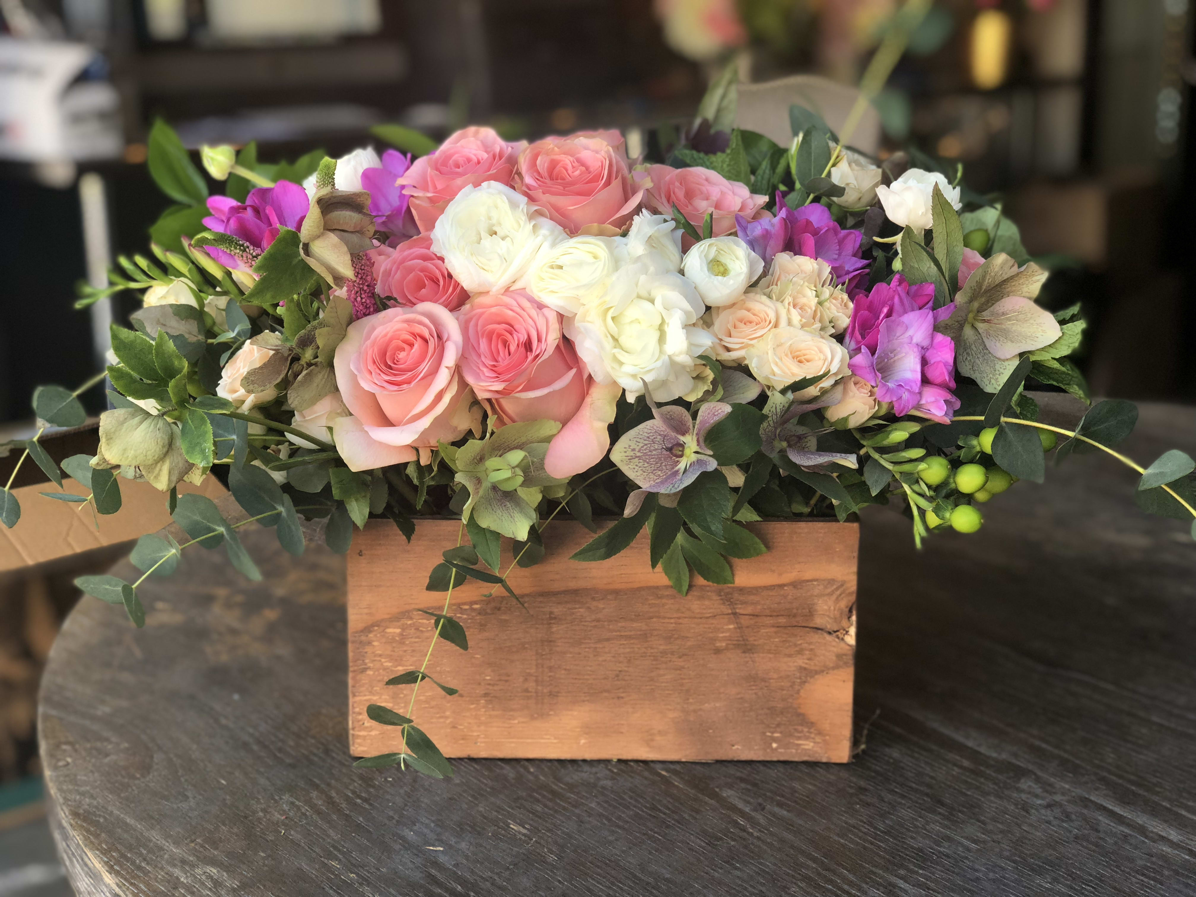 Dolce Mamma - Discover the beauty and fragrance of this stunning design! Featuring Amsterdam pink roses, ranunculus, veronica, ,mint, eucalyptus, and more, artfully arranged in a charming woodland box. This arrangement not only captivates with its vibrant colors but also delights the senses with its enchanting fragrance. Perfect for adding a touch of natural elegance to any setting or gifting to someone special. Order now to bring the essence of a lush garden into your home or event!