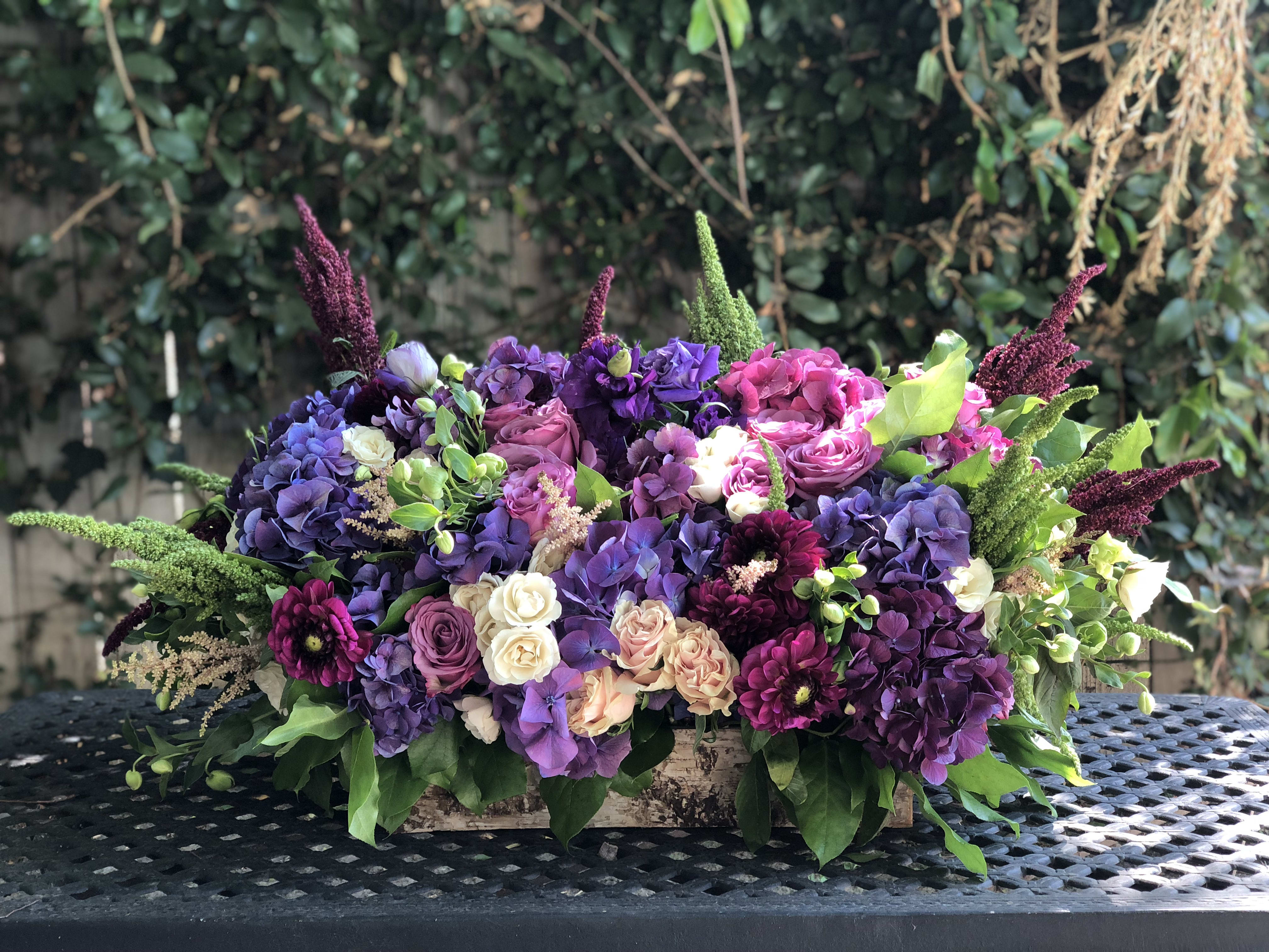Low floral arrangement of purple, pink, and white blooms in a wooden box