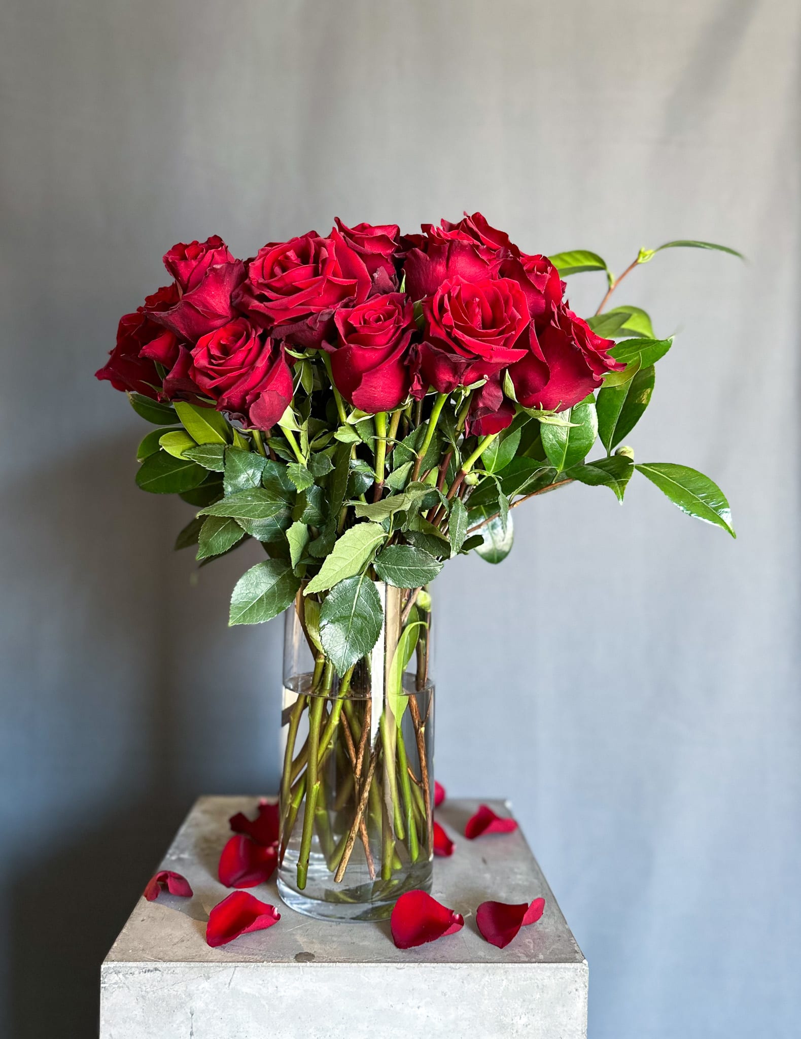 Red roses in a clear glass vase with scattered petals