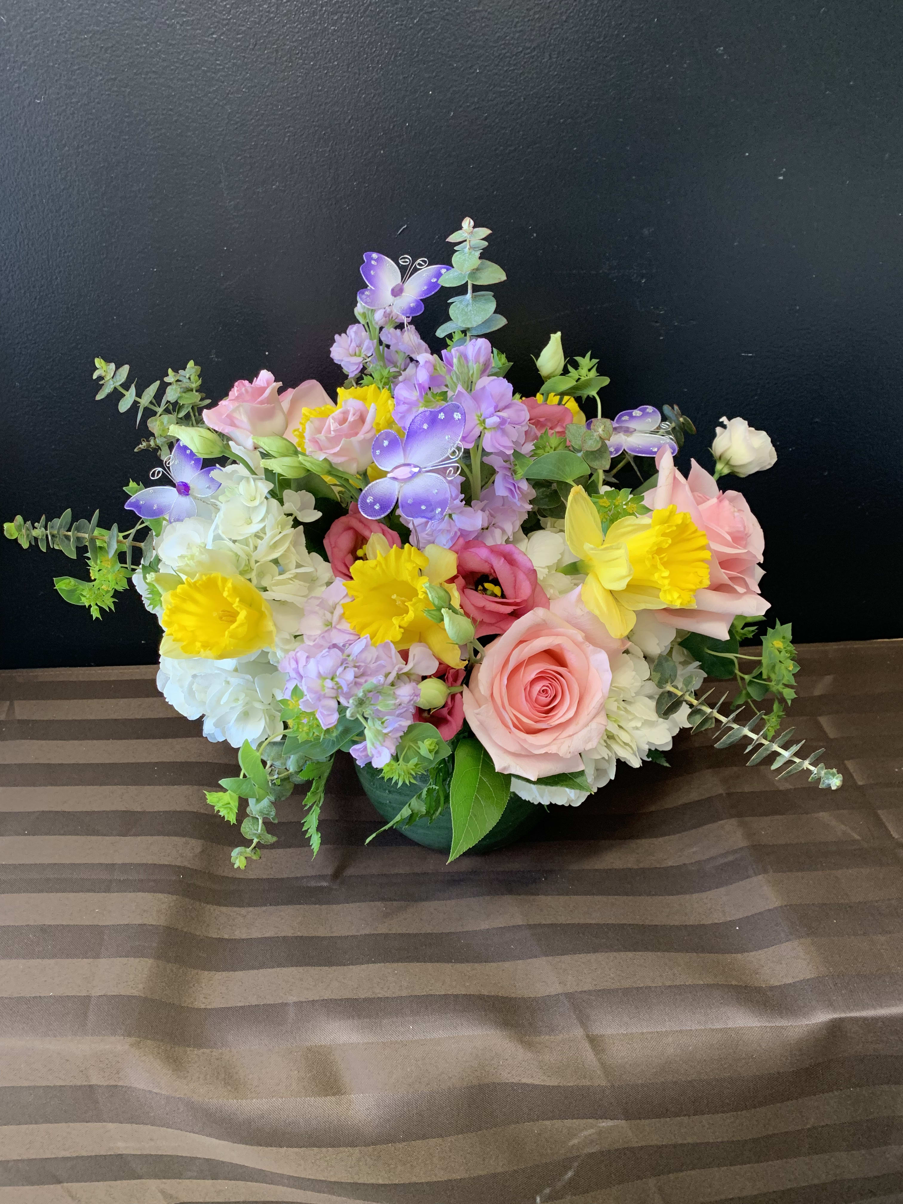 Mixed bouquet of pink, yellow, white, and purple flowers in a low container