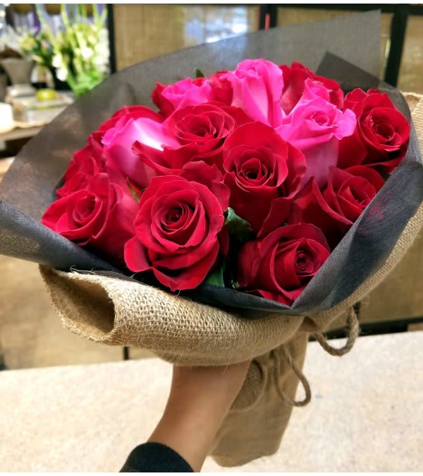 Hand-tied bouquet of red and pink roses wrapped in black paper and burlap