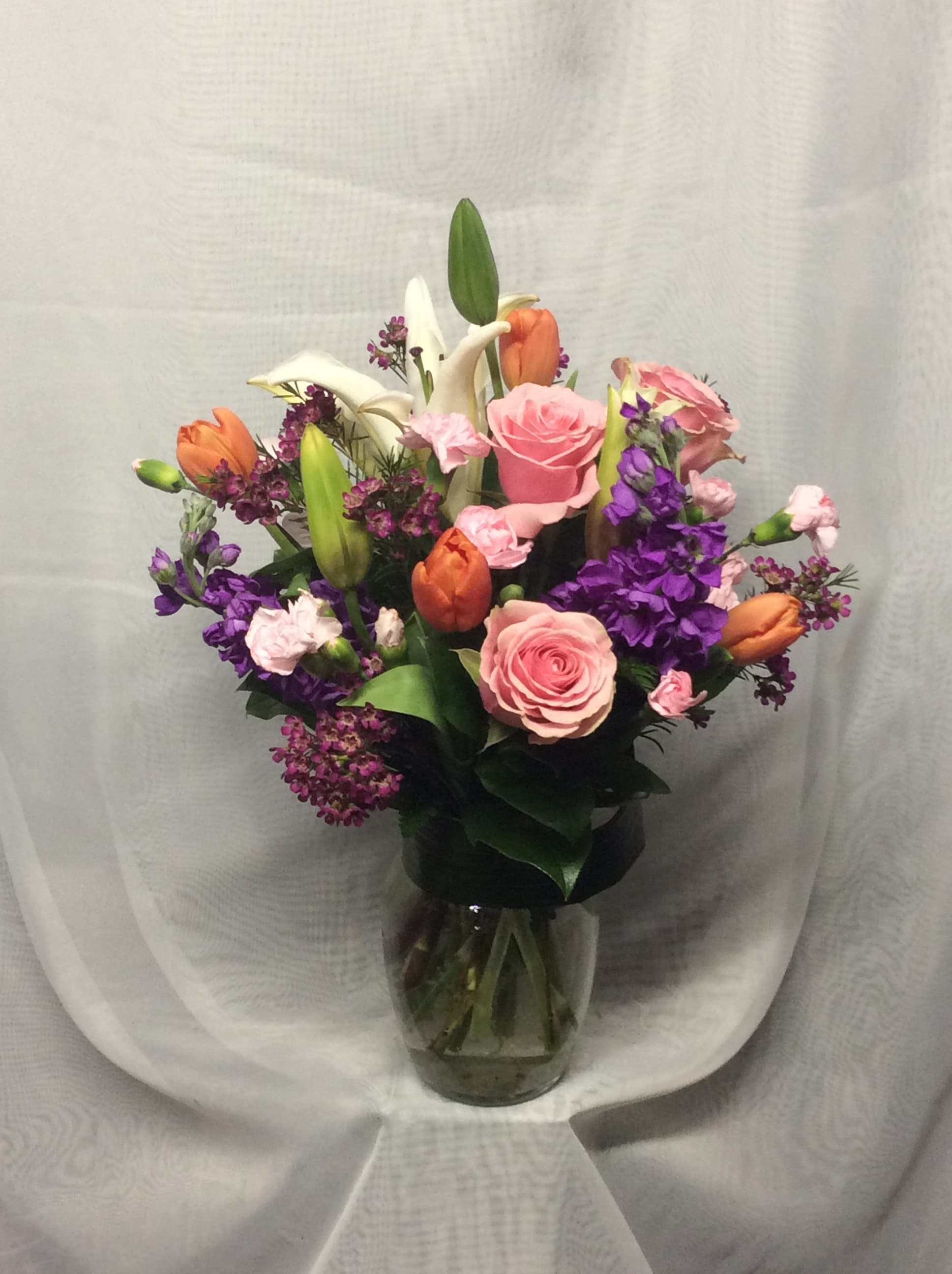 Mixed bouquet of pink roses, orange tulips, white lilies and purple flowers in a clear glass vase