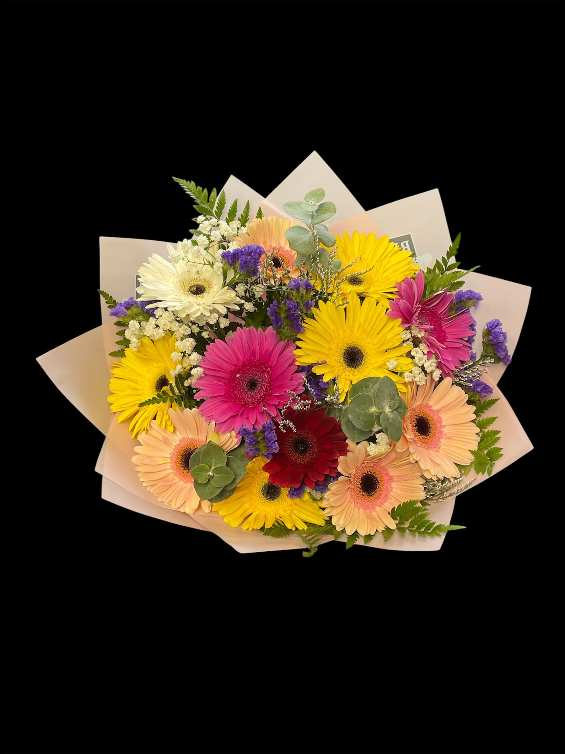 Hand-tied bouquet of multicolored gerbera daisies with white and purple accents wrapped in pale paper