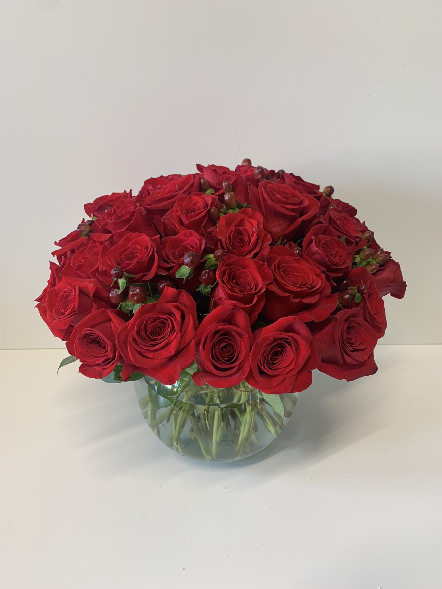 Low round arrangement of red roses with berries in a clear glass bowl vase