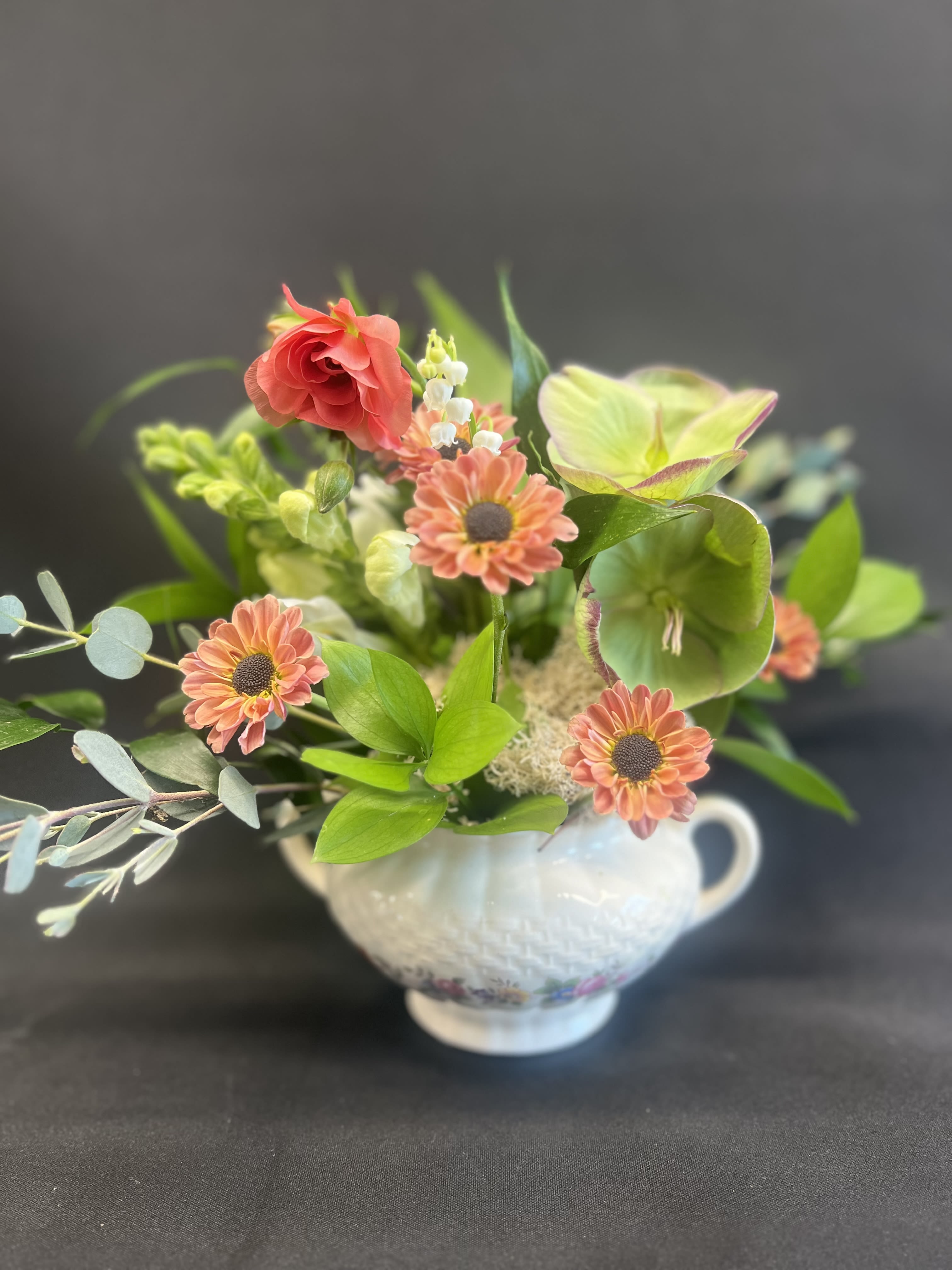 Mixed floral arrangement in a white handled vase with coral and green blooms