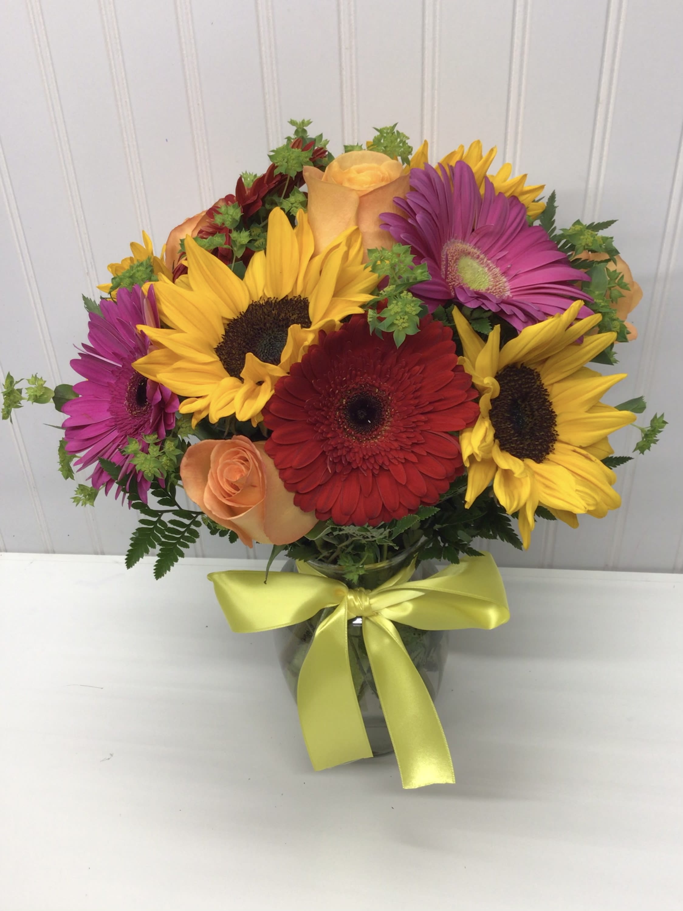 Bouquet of sunflowers, gerbera daisies, and roses in a glass vase with a yellow ribbon