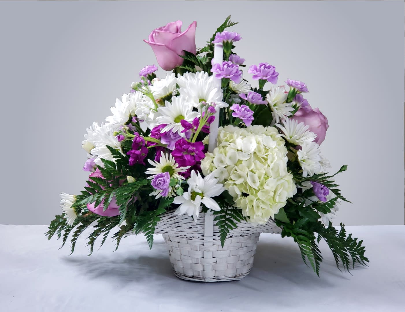 Pink roses, white daisies, and purple flowers in a white basket
