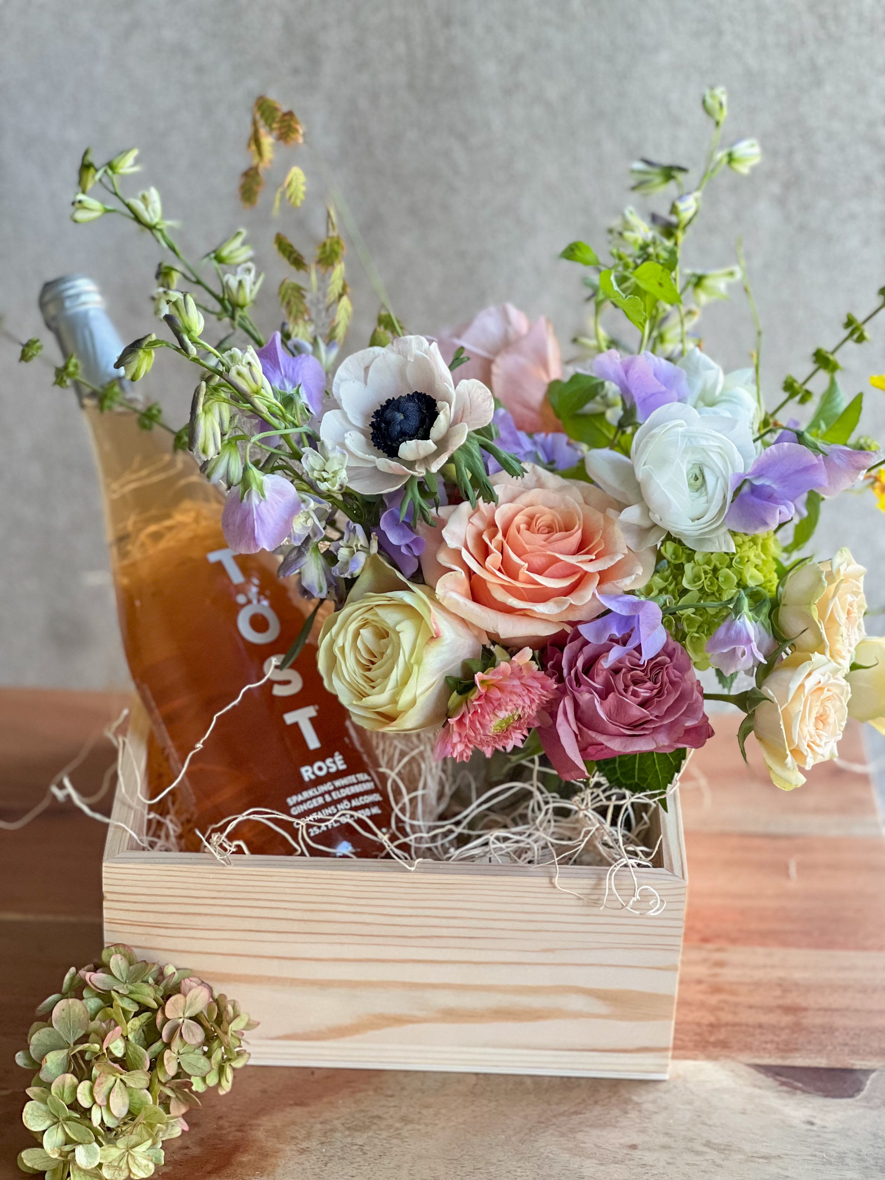 Mixed pastel bouquet in a wooden box with a bottle of rosé