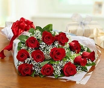 Bouquet of red roses wrapped in white paper with a red bow