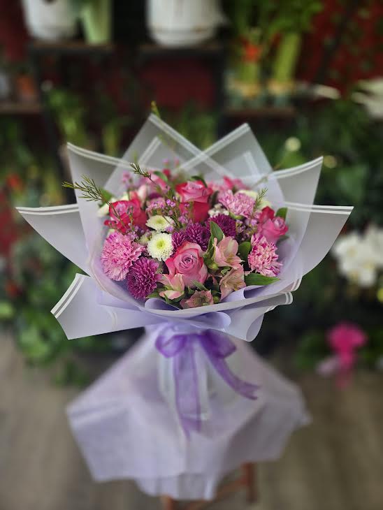 Pink and purple mixed bouquet wrapped in white paper with a purple ribbon