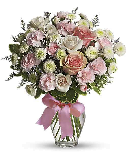 Cotton Candy Bouquet - A dreamy pastel mix of pale pink and ivory roses makes this flower arrangement feel like a gentle hug - perfect as a birthday bouquet or a get-well gift that says you care. The Cotton Candy Bouquet brings together roses, soft pink carnations, and small white button chrysanthemums with sprigs of lavender filler to create a rounded, airy composition that reads feminine and comforting for anniversaries, new babies, or just-because surprises.  The flowers are gathered in a clear glass vase that showcases the straight stems and is finished with a wide pink satin ribbon tied in a bow for an elegant, tactile detail. Colors move softly between pink, white, green foliage, and hints of lavender; textures range from velvety rose petals to the ruffled carnations and tiny, cushiony mums, giving the bouquet visual depth and a light, fragrant presence.  This arrangement is made to make the recipient feel truly seen - tender, celebrated, and comforted. Standard vase height and the full rounded shape make it an easy centerpiece for a bedside table or dining room - no extra styling needed. Care: keep in fresh water, trim stems every few days, and keep away from direct heat to extend bloom life.