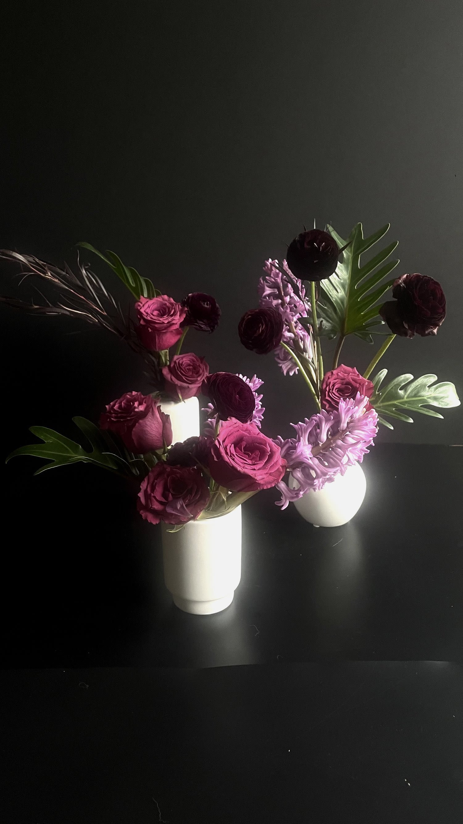 Two floral arrangements in white vases with pink and burgundy blooms