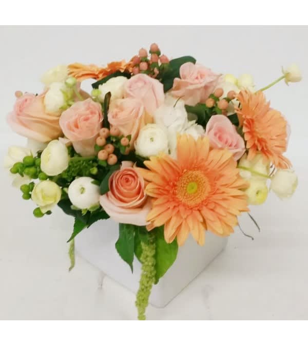 Peach and white bouquet with gerbera daisies and roses in a white container