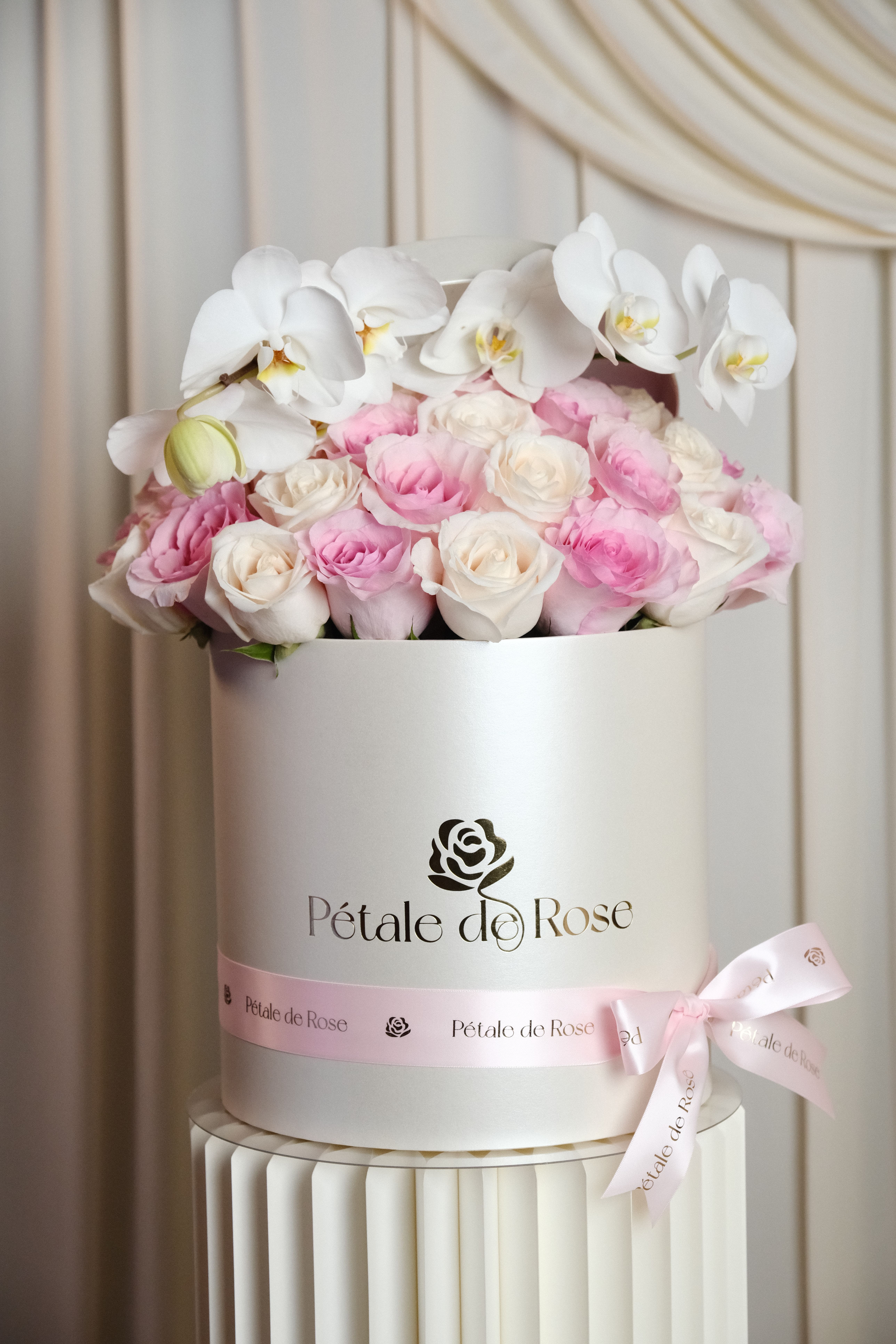 Bella - A timeless luxury arrangement featuring blush and ivory roses topped with elegant white  orchids in our signature pearl box.  Designed with softness, sophistication, and femininity in mind, this arrangement creates a graceful floral statement perfect for Mother’s Day gifting.  Please note: Flower substitutions and shades may vary based on seasonal and market availability. Our designers will always maintain the overall color palette, freshness, style, and luxurious feel of the arrangement shown.