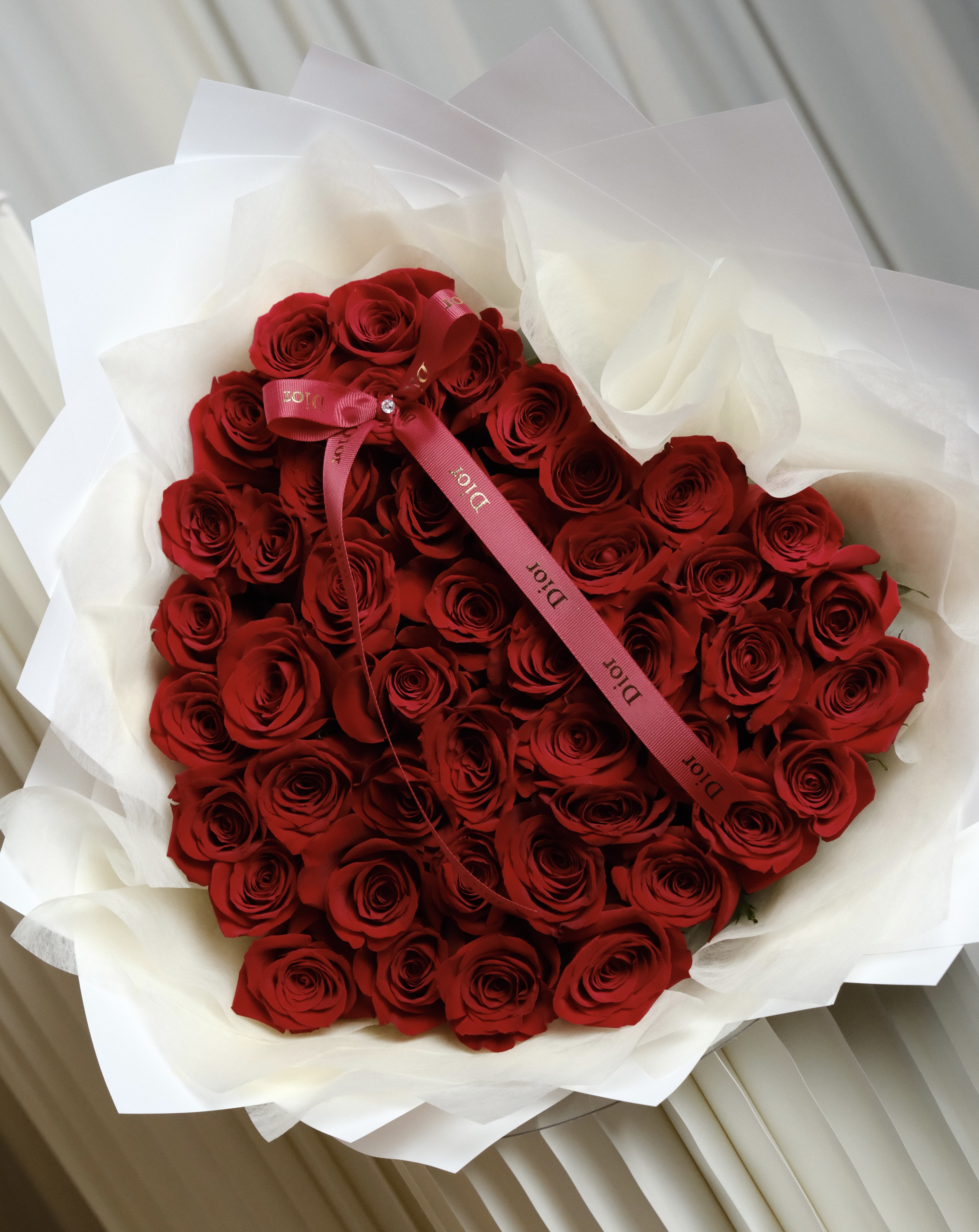 Large bouquet of red roses wrapped in white paper with a pink ribbon