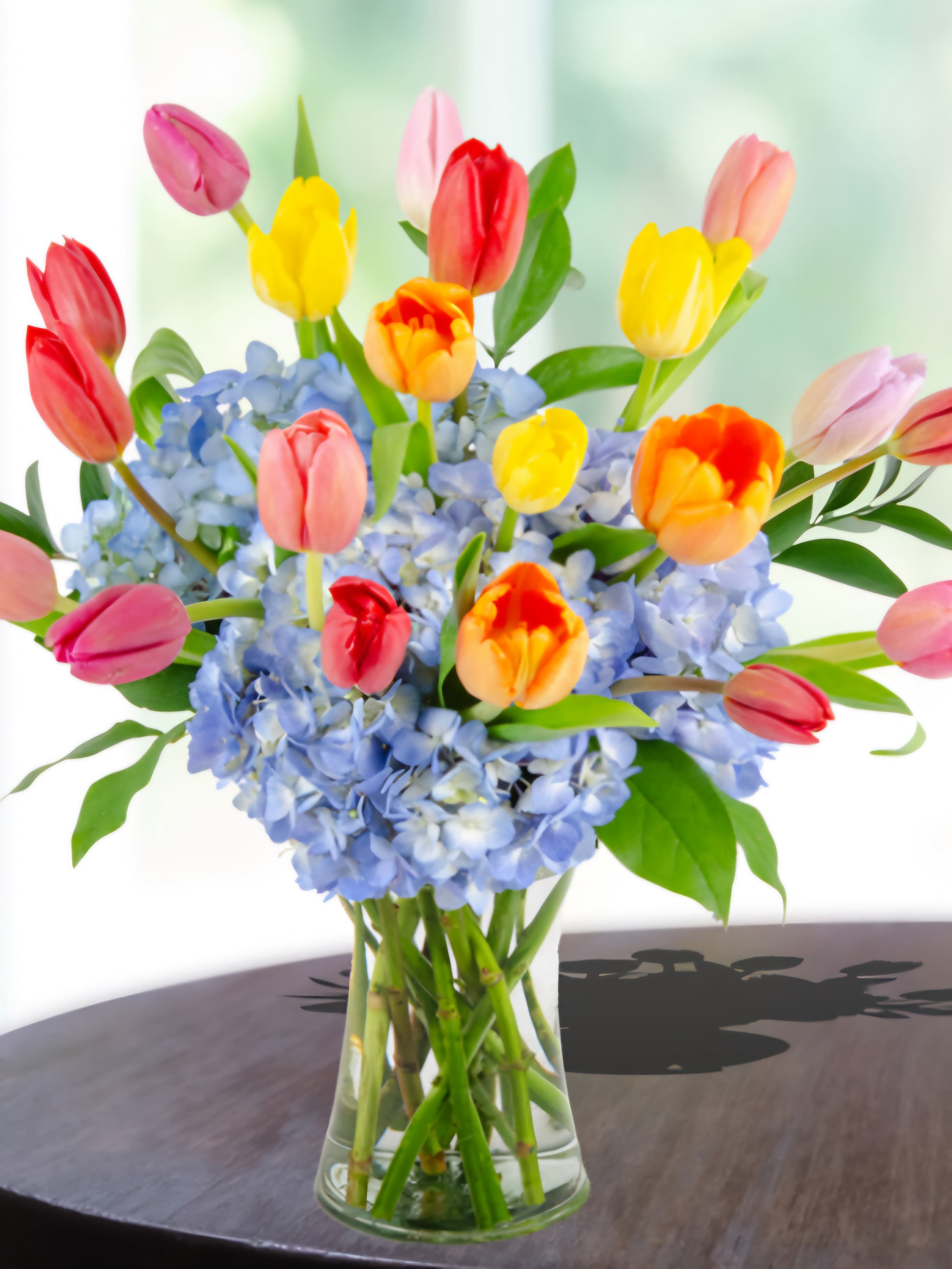 Colorful tulips arranged in a glass vase with blue hydrangeas