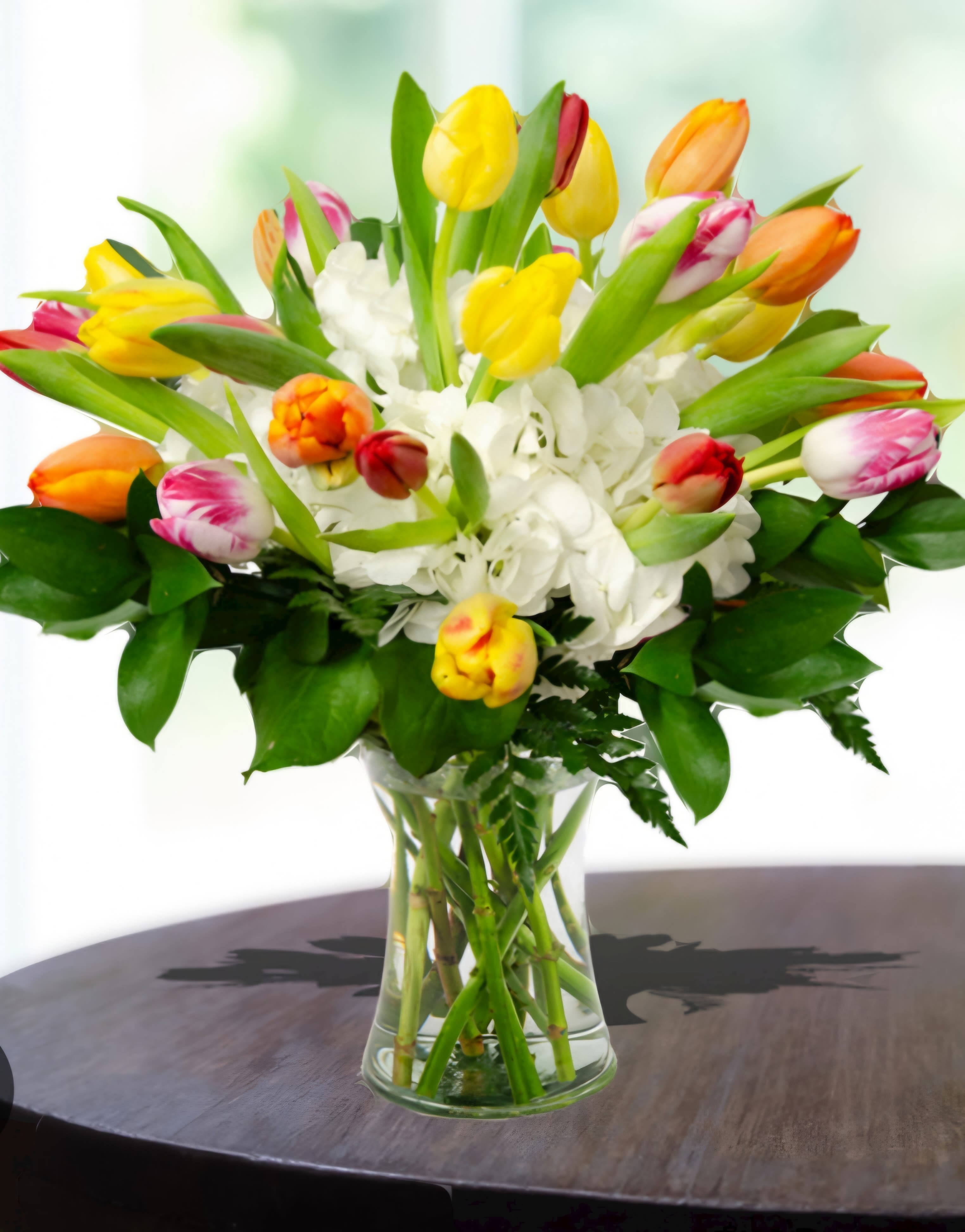 Bouquet of multicolored tulips and white hydrangeas in a clear glass vase