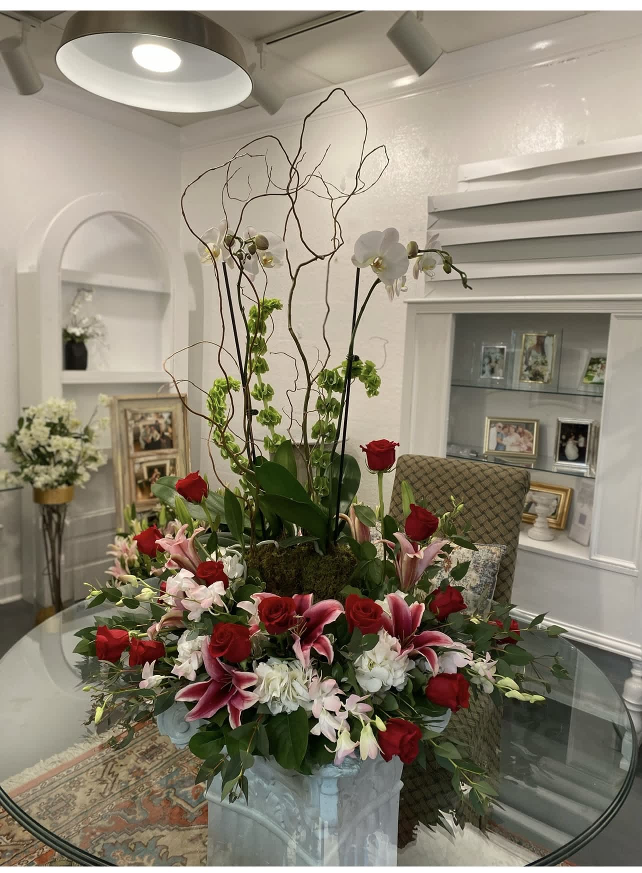 Tall floral arrangement with red roses, pink lilies, and white orchids in a pedestal vase